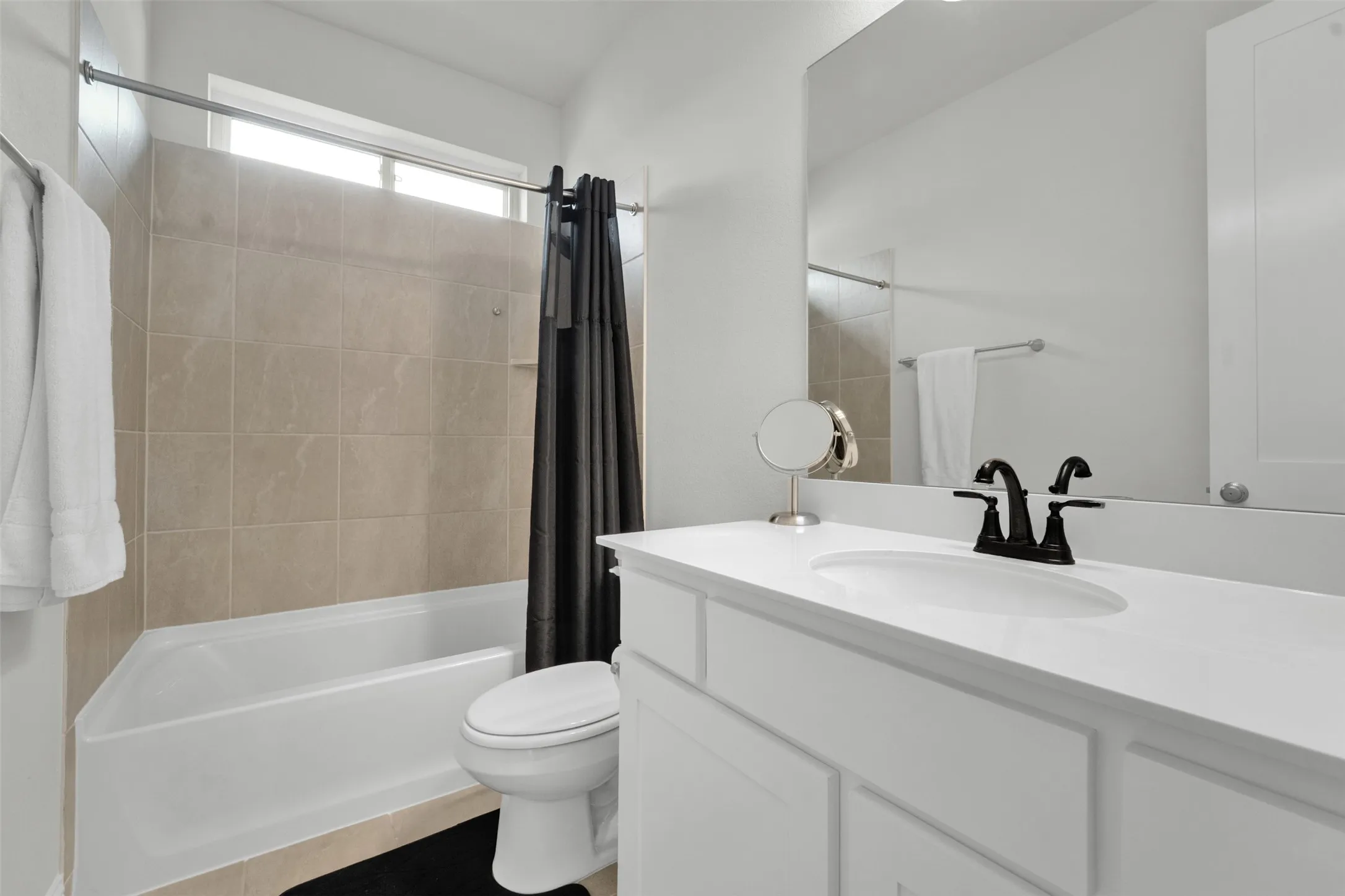 Bathroom featuring a single vanity with an integrated sink, black hardware, a framed mirror, and white cabinetry