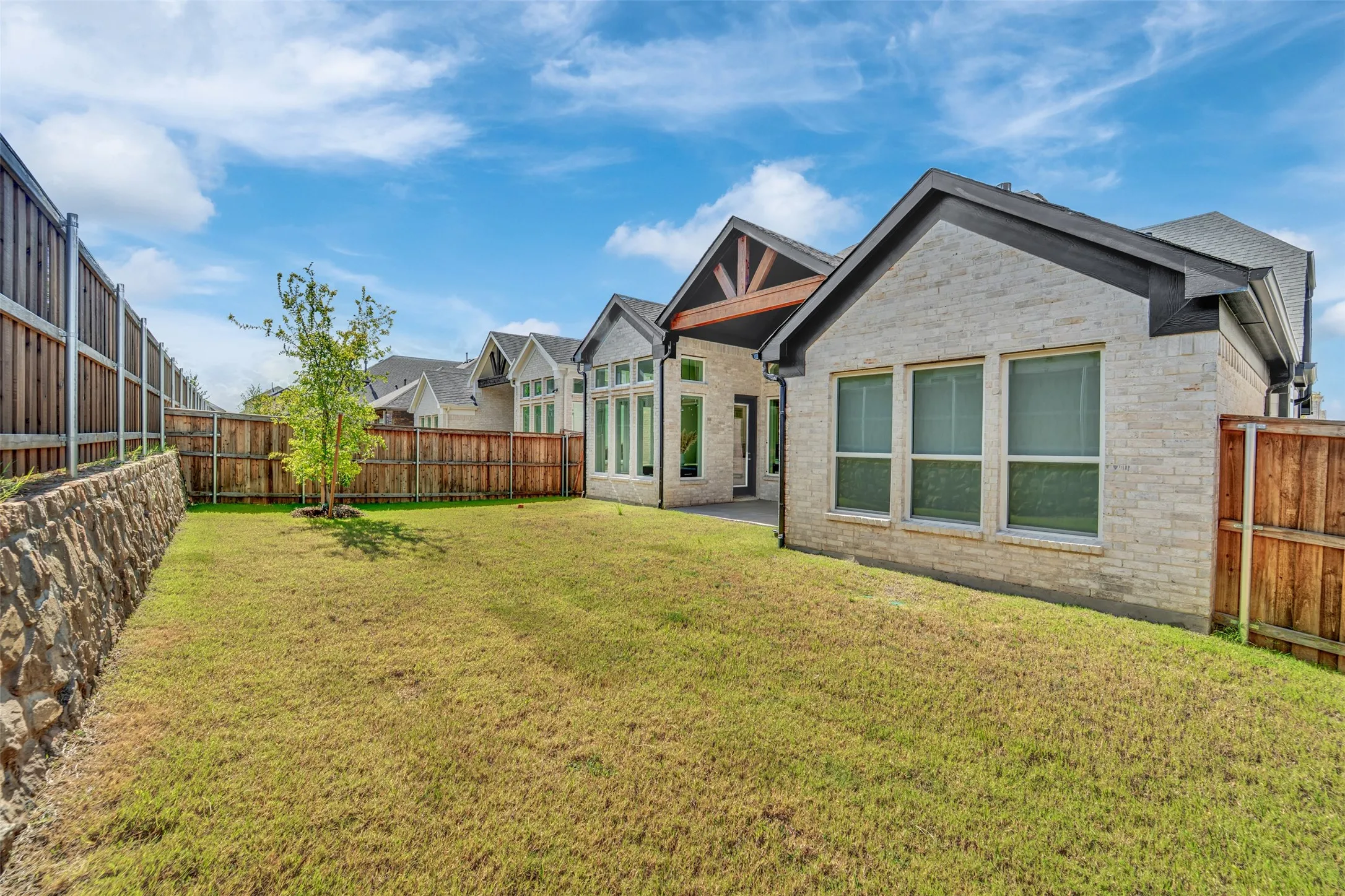 Expansive grassy lawn with a young tree, bordered by a wood fence and a stone retaining wall