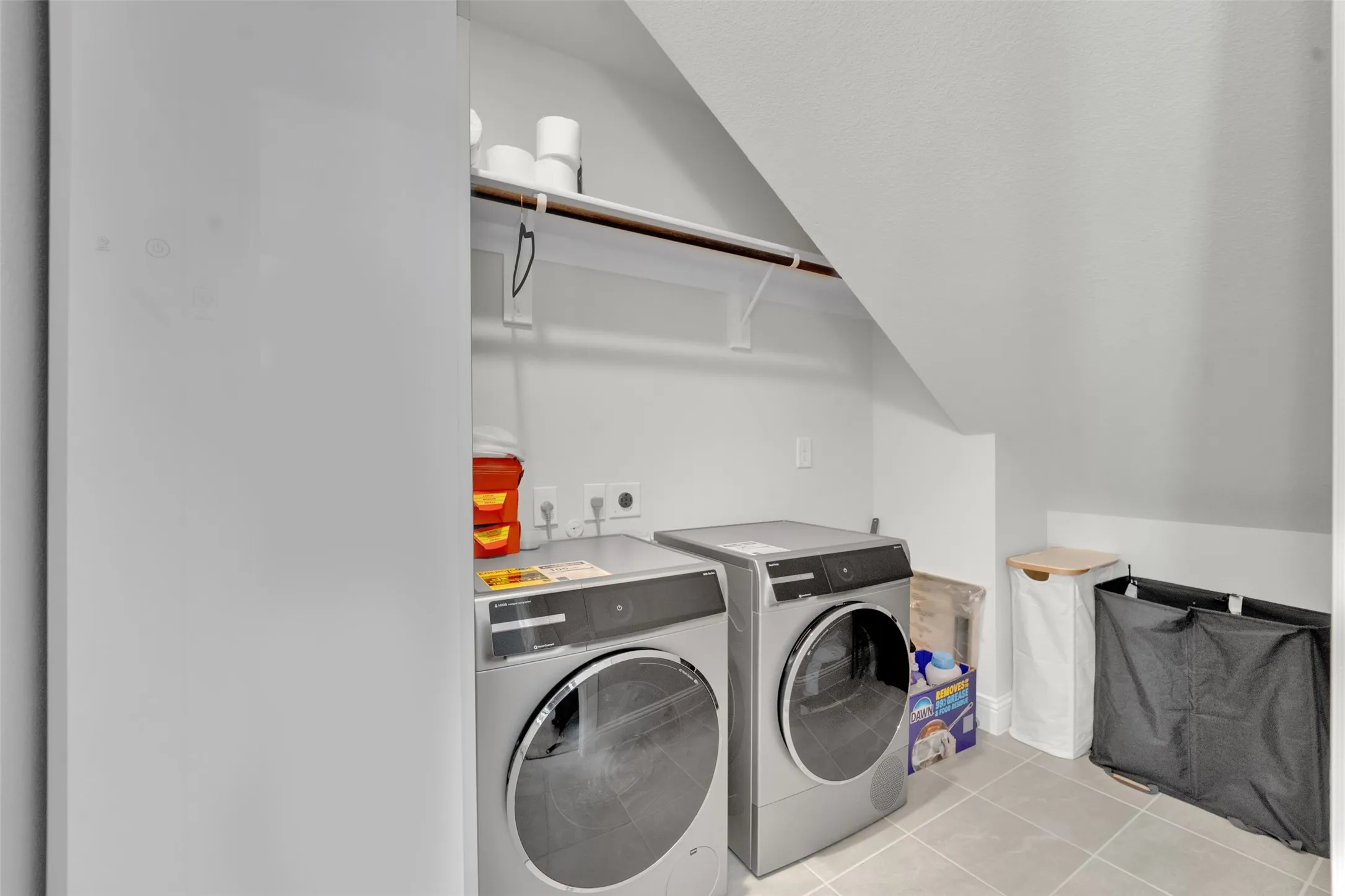 Laundry area featuring slate-style floor tiling, a built-in shelf with hanging rod, and sloped ceiling architecture