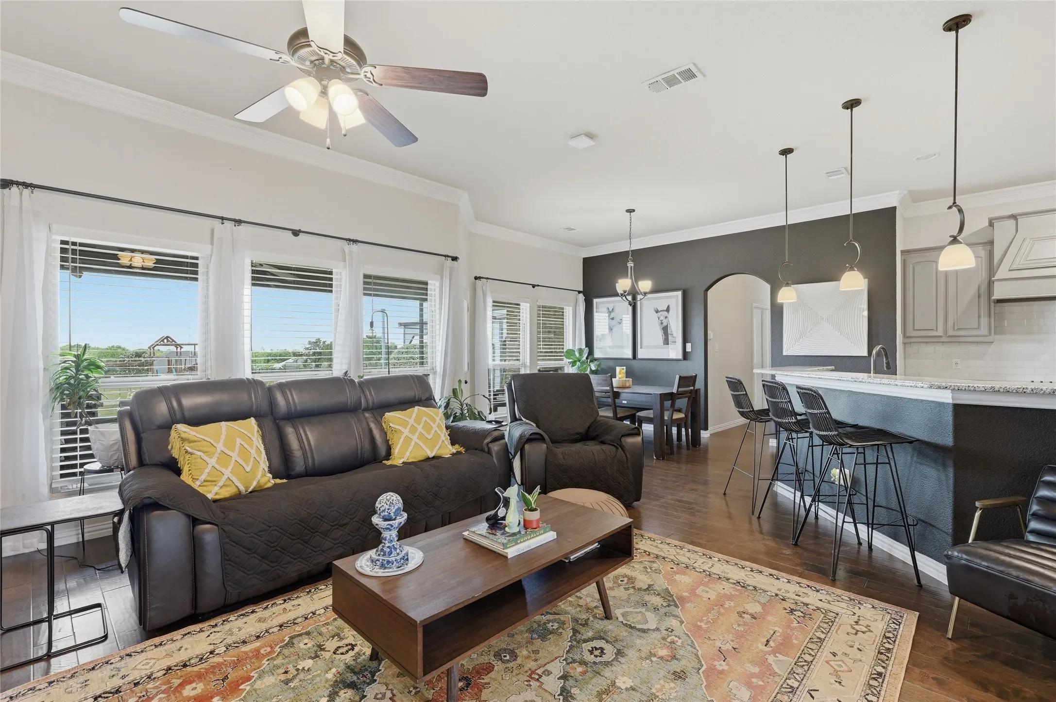 Spacious living area featuring wood-finish flooring, ample natural light from multiple windows, and a ceiling fan