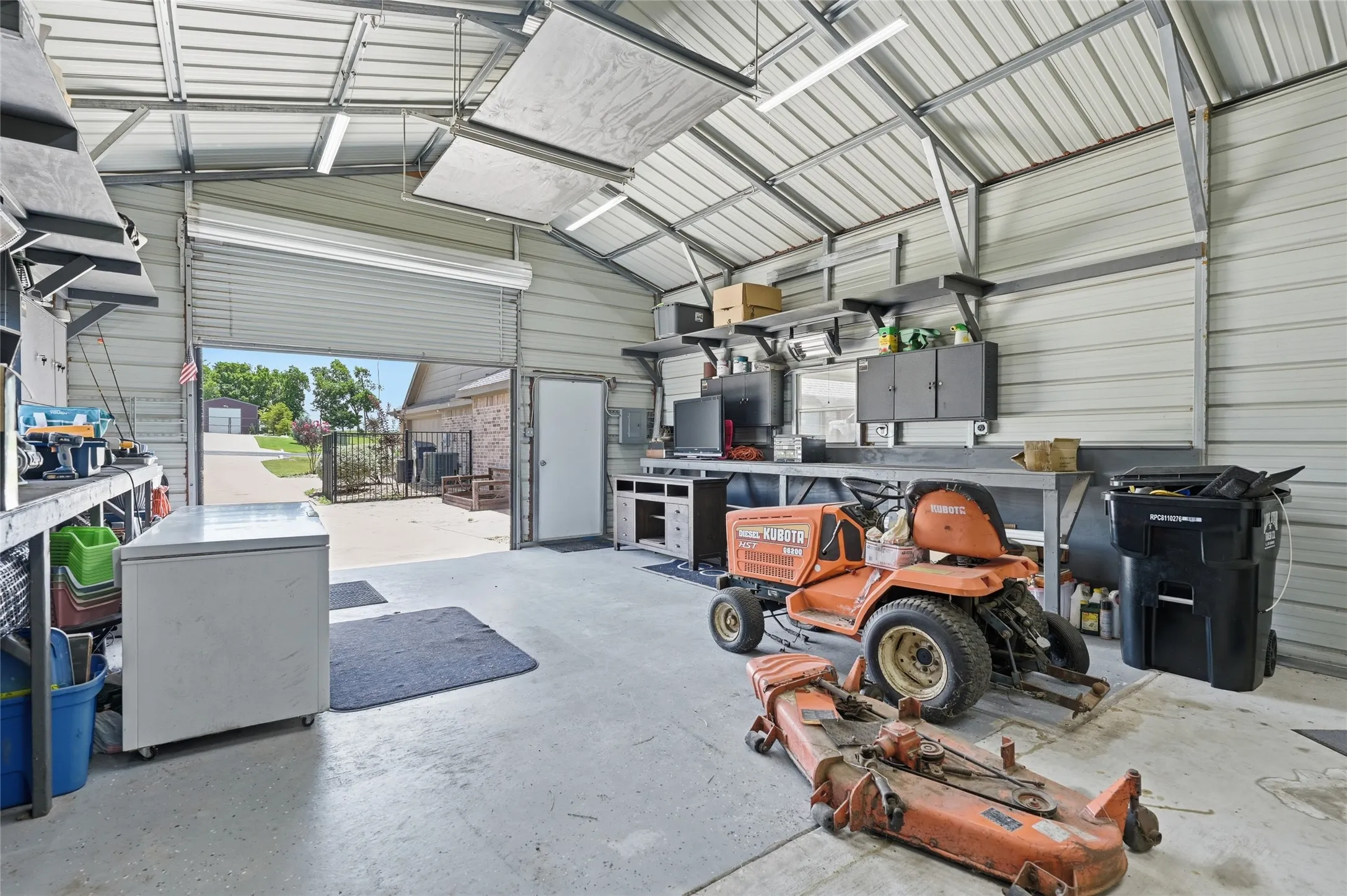 Spacious detached workshop featuring a roll-up door, side entry door, concrete flooring, and extensive built-in workbench with storage
