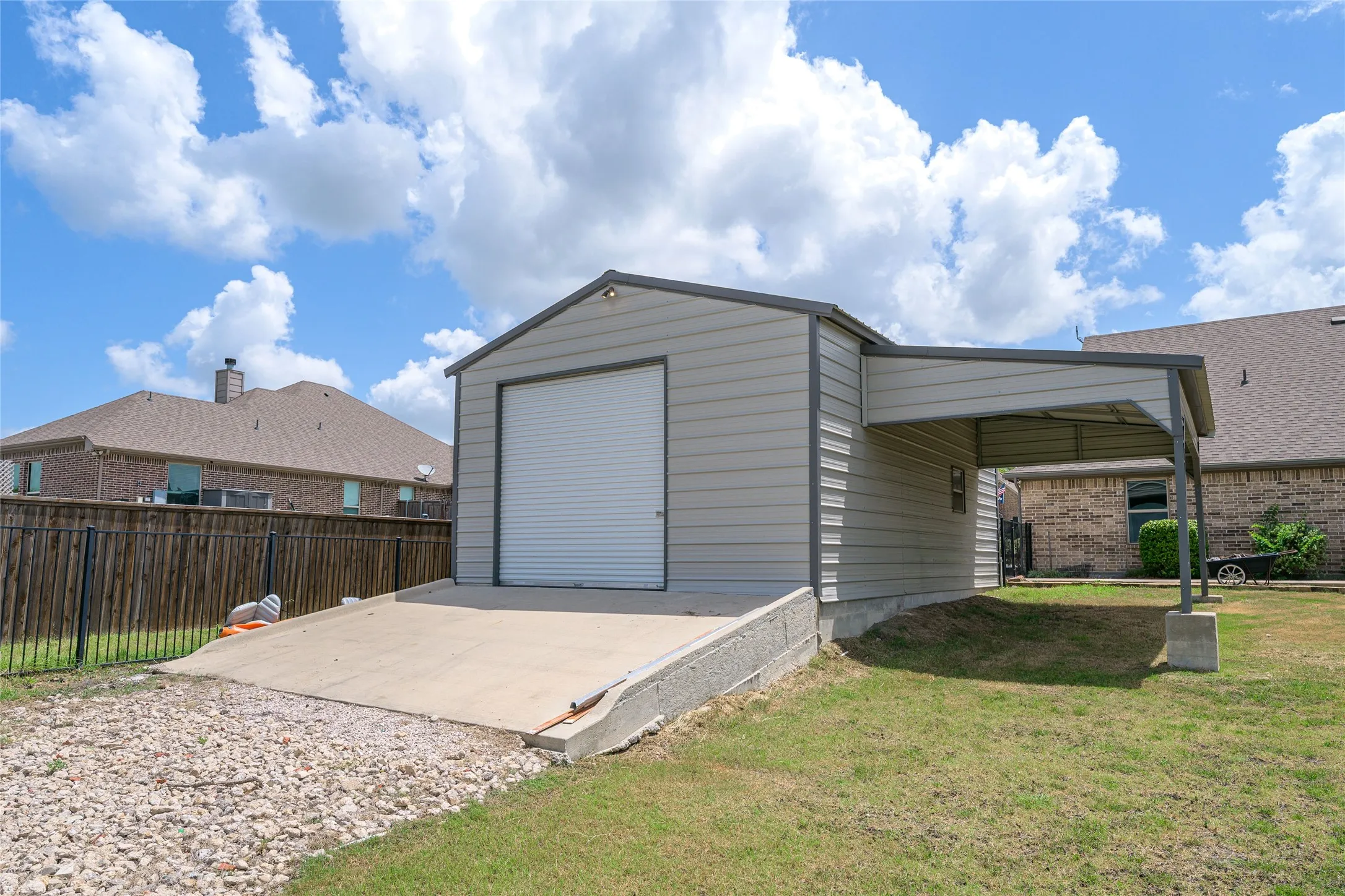 Detached metal utility building with a roll-up door, concrete ramp, and an attached metal carport