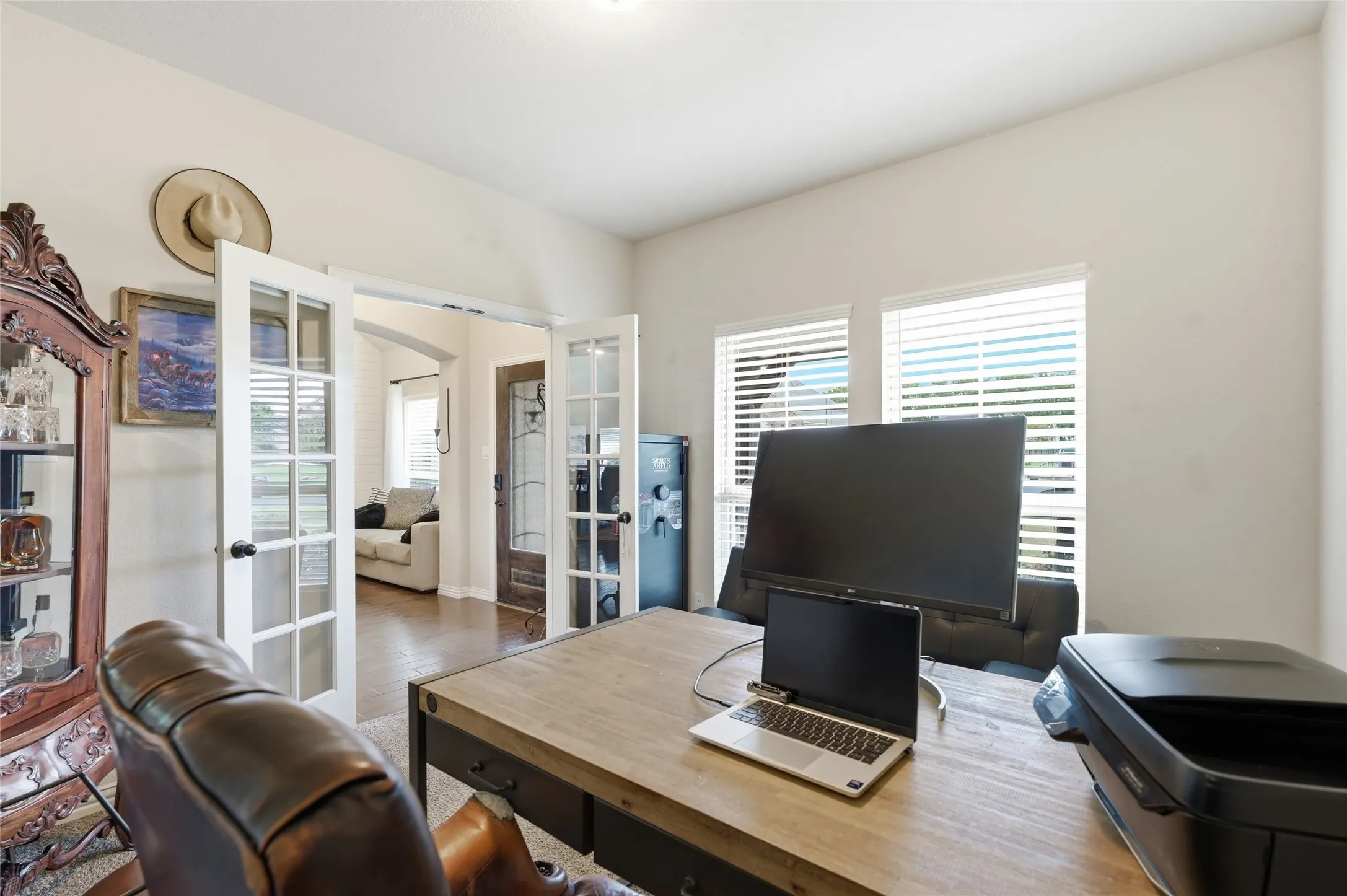 Bright interior space featuring wood-finish flooring, white French doors, and two windows with horizontal blinds