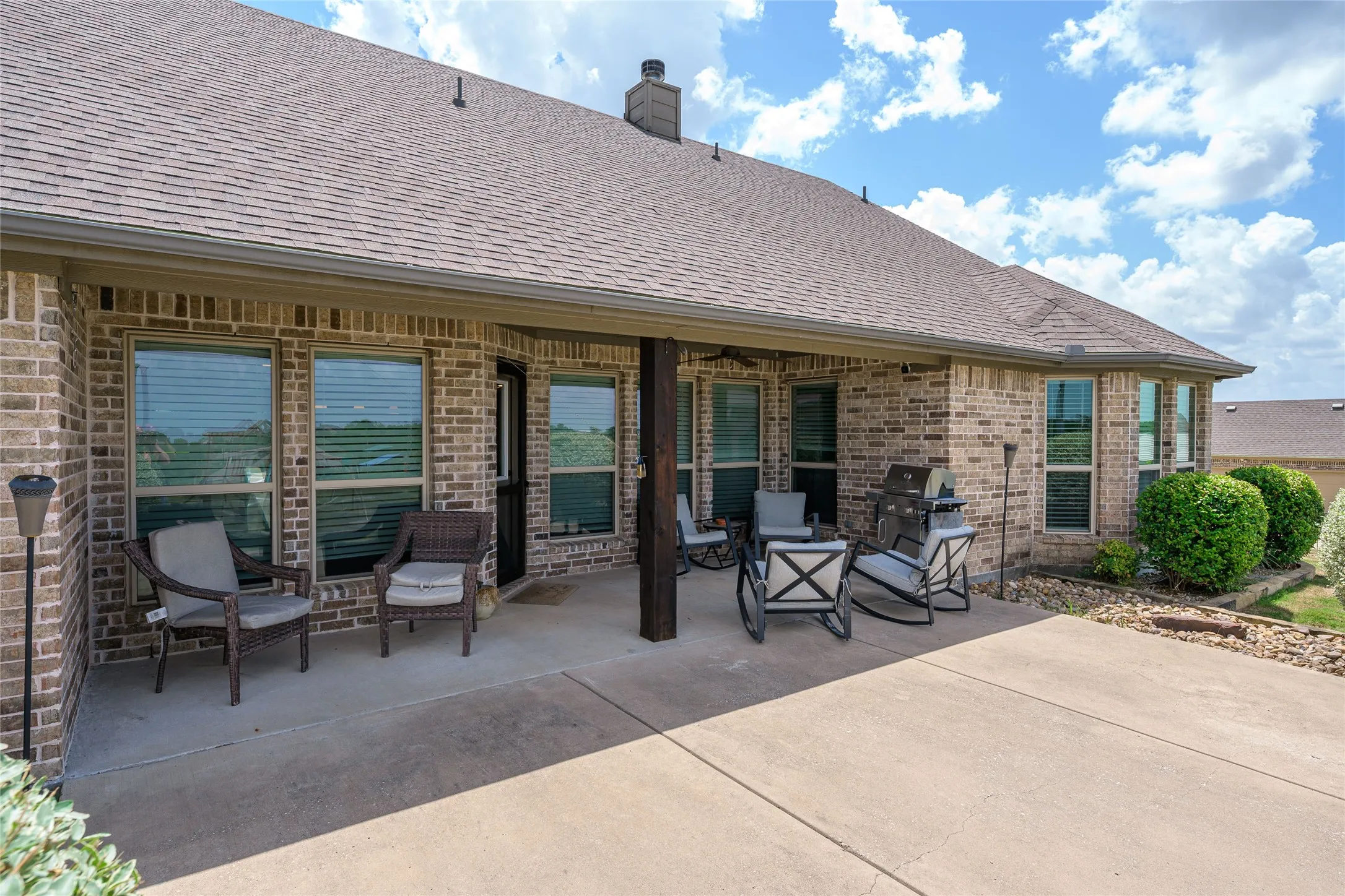 Expansive brick exterior featuring a covered patio, concrete slab, and mature landscaping