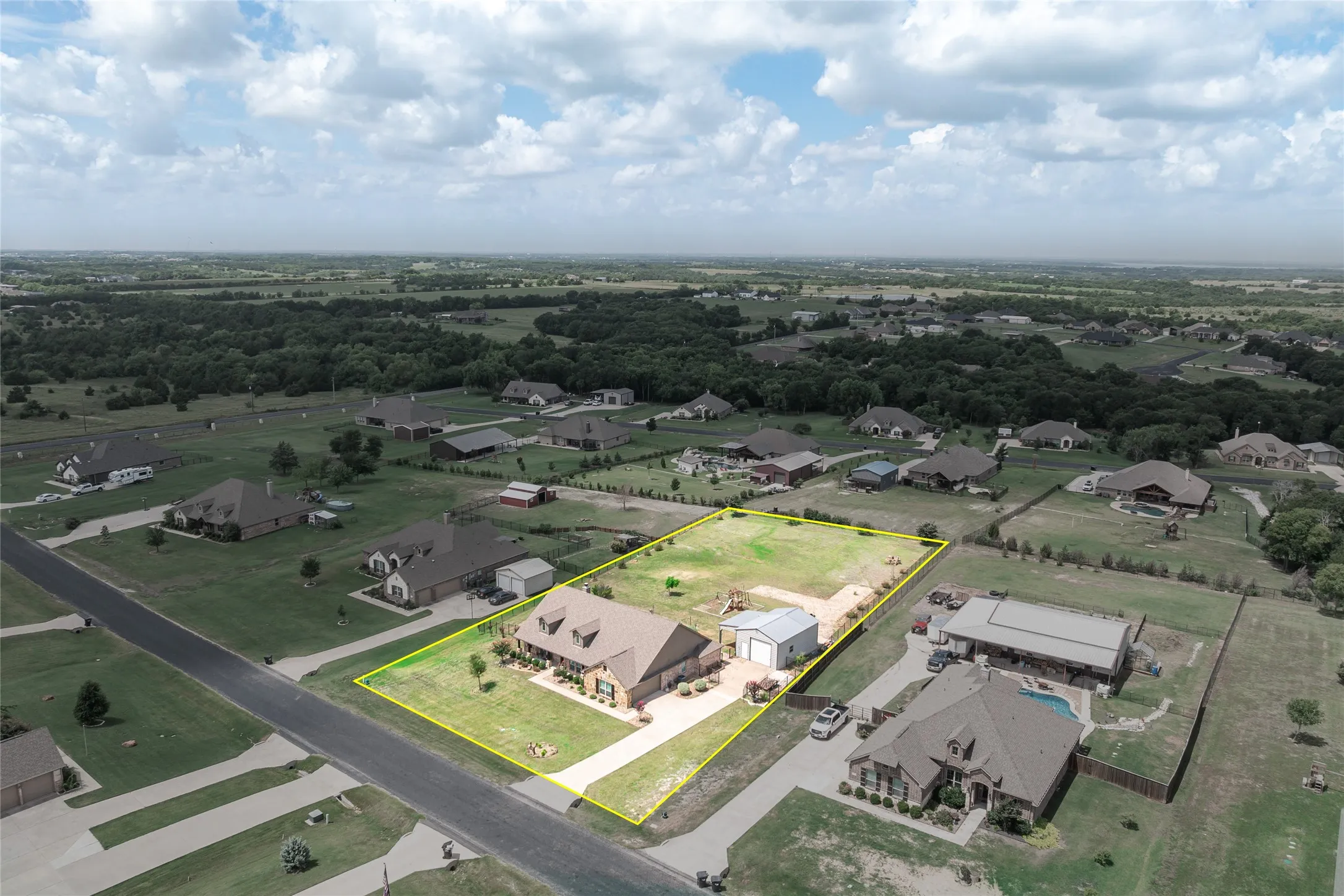 Aerial perspective showcasing a single-story brick residence with an attached garage and a detached metal building