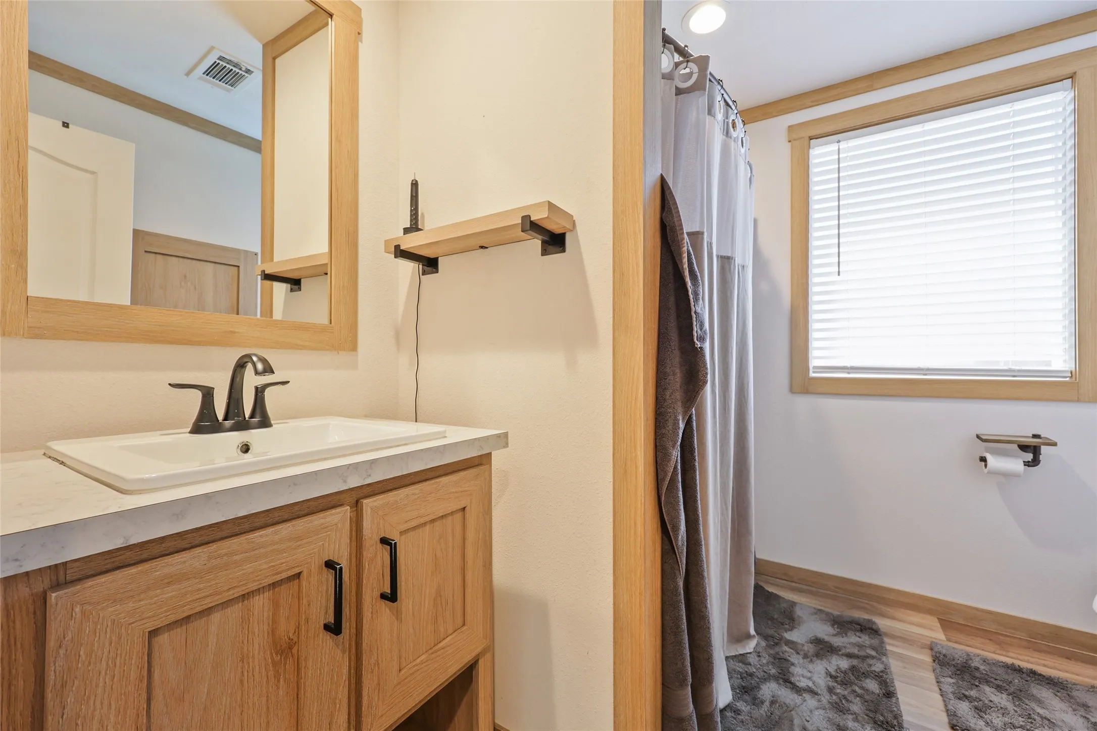 Bathroom featuring a light wood-finish vanity with a white rectangular sink, a black faucet, and a framed mirror