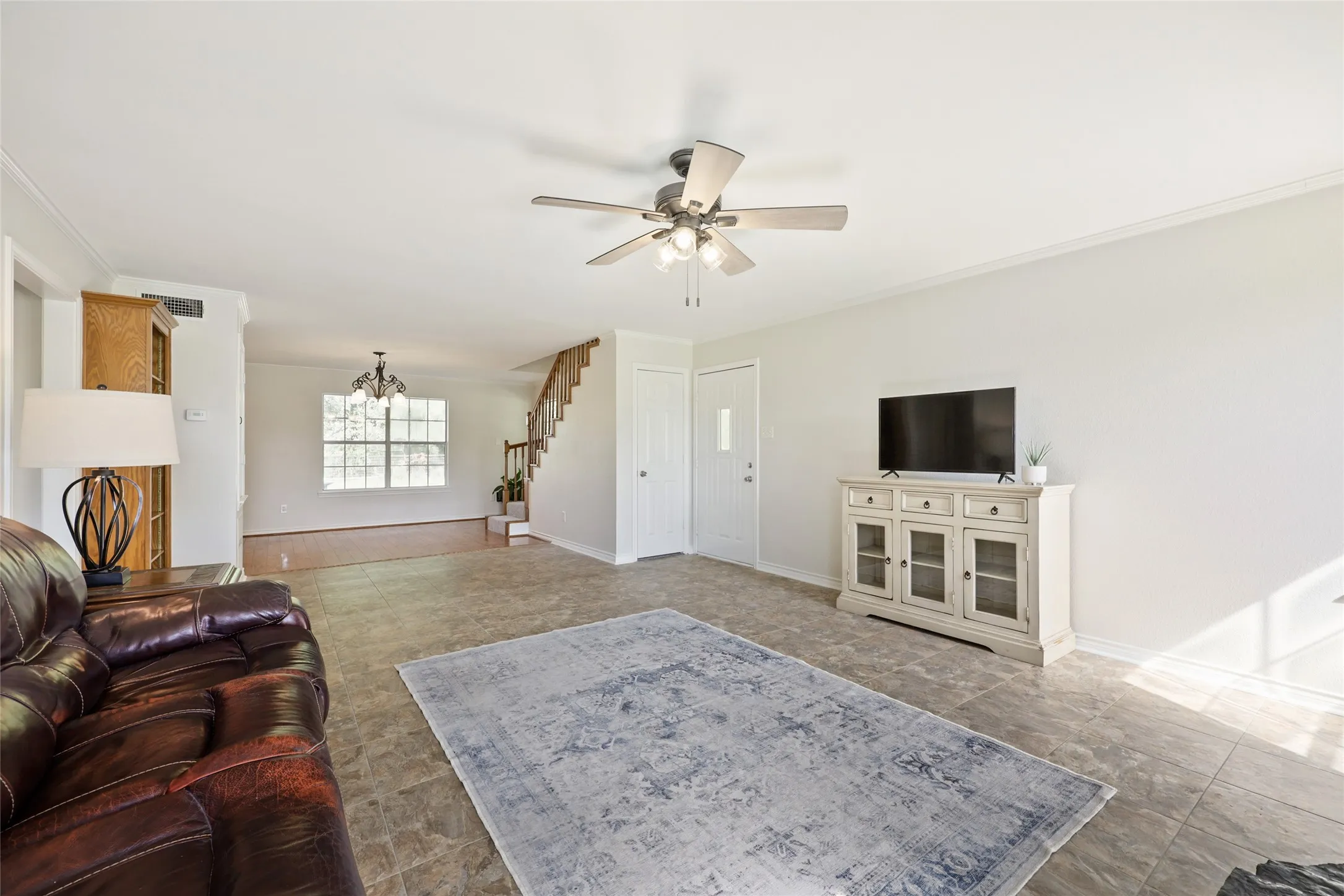 Spacious living area featuring neutral wall tones, tile flooring, a ceiling fan with integrated lighting, and crown molding