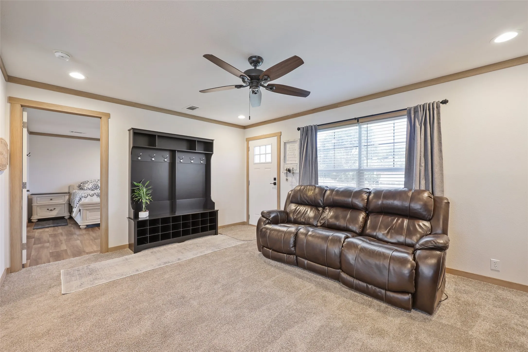 Carpeted living area featuring a ceiling fan with integrated lighting, recessed lighting, and a white entry door with a window pane