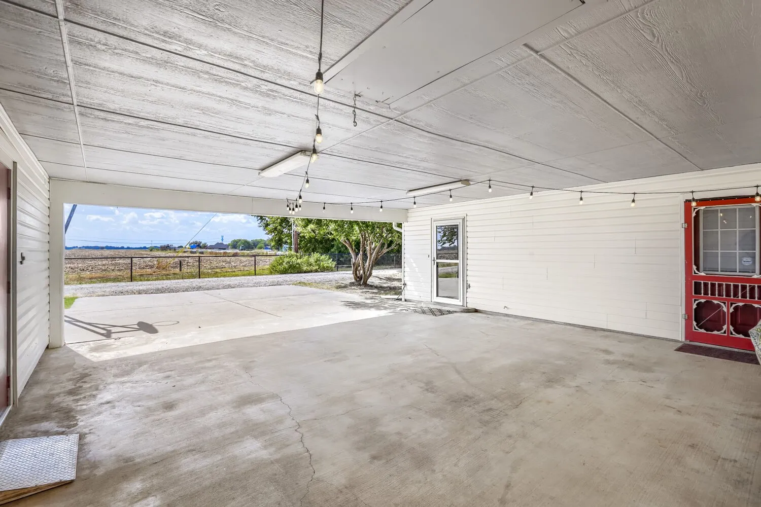 Spacious covered concrete patio with white wood-paneled ceiling, string lighting, and white horizontal siding