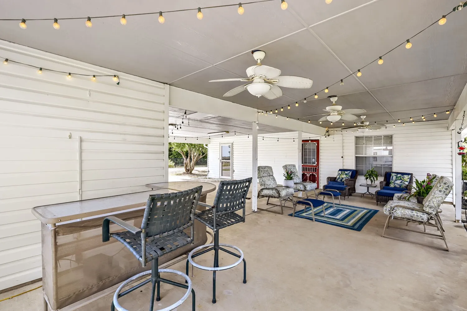 Spacious covered patio featuring string lighting, multiple ceiling fans, and a bar area