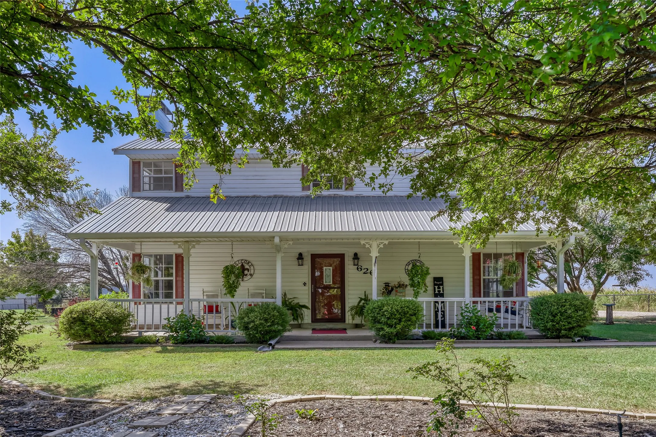 Two-story white siding residence featuring a metal roof, a full-width covered front porch with white railings, and red window shutters