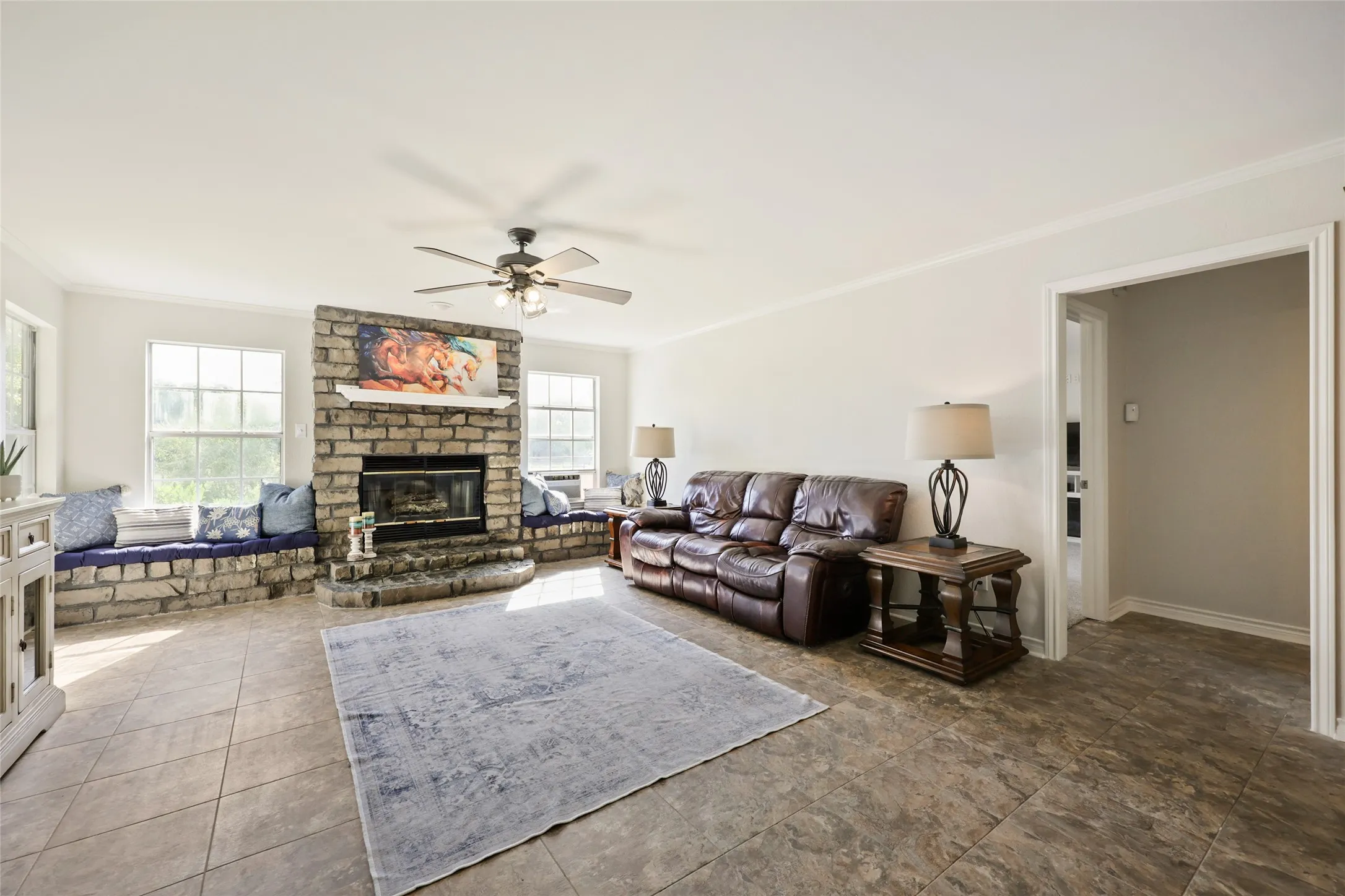 Spacious living area featuring stone fireplace with hearth, multiple windows, and tile flooring