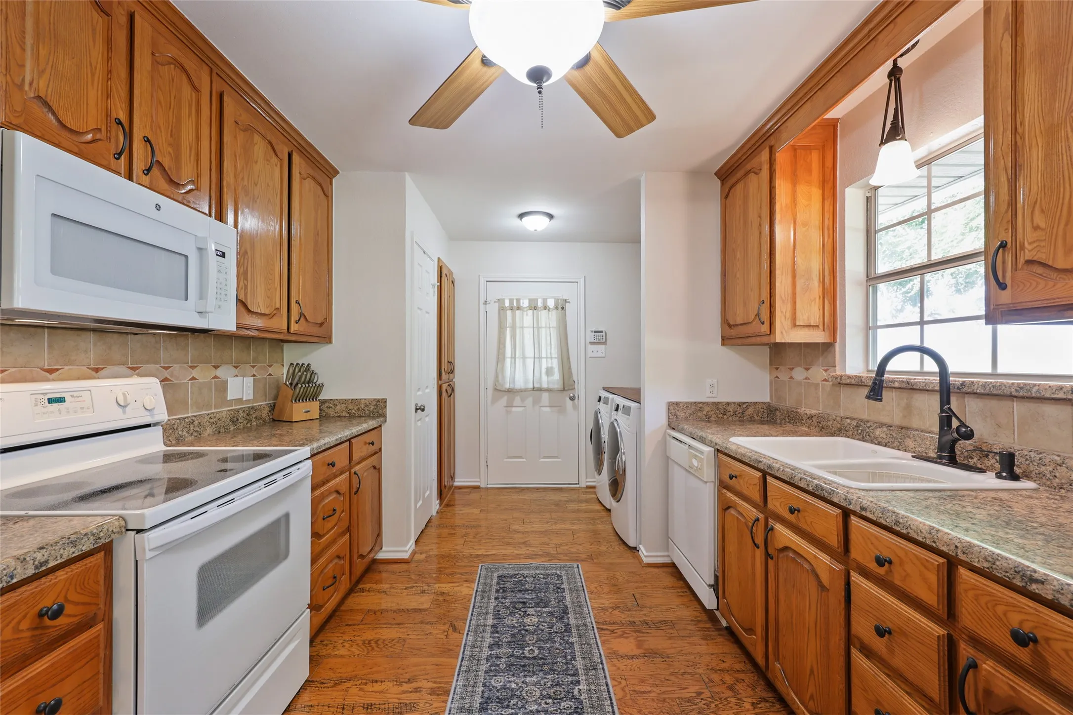 Expansive kitchen featuring wood-finish flooring, abundant wood cabinetry, durable countertops, and an integrated white dual-basin sink with a gooseneck faucet