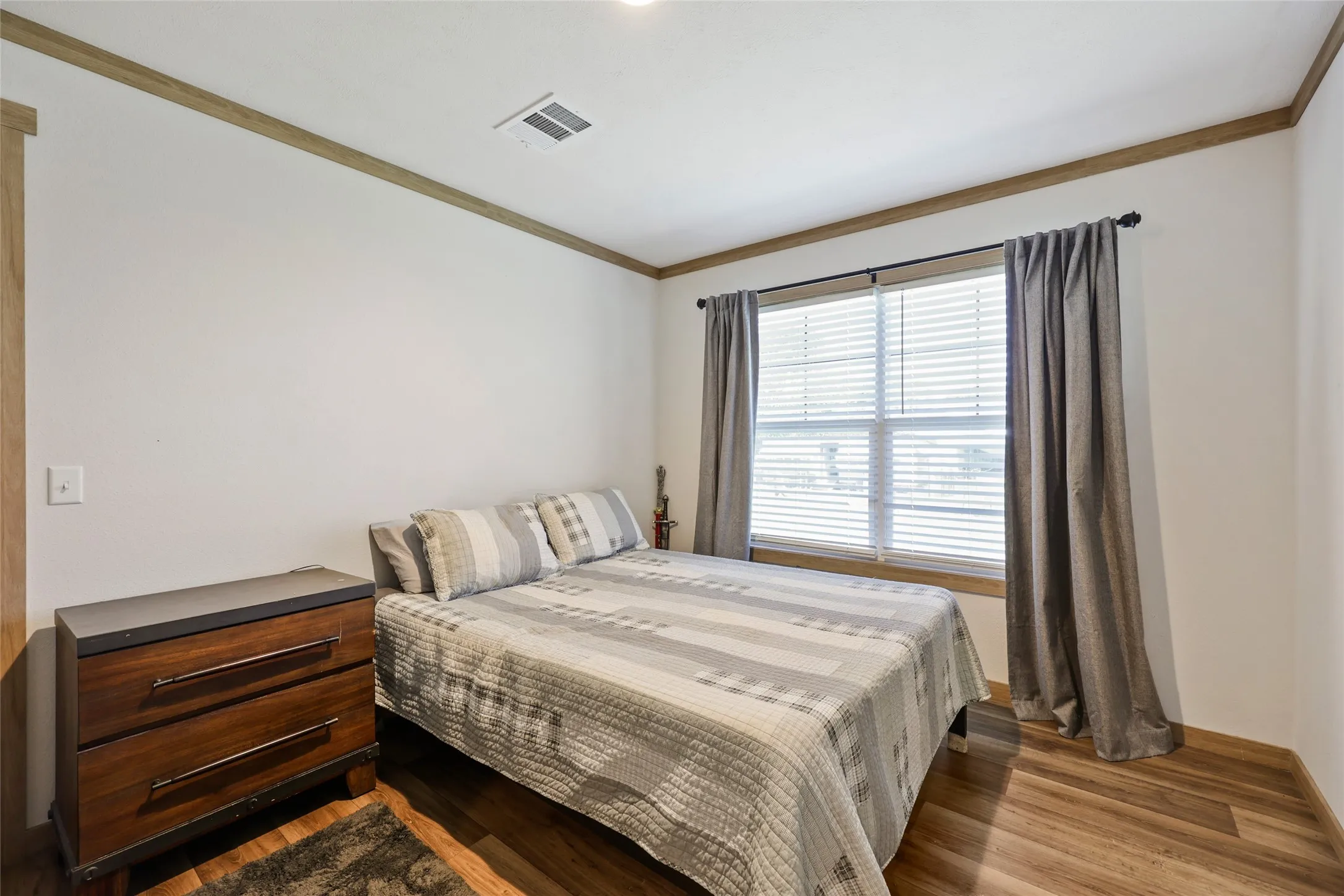 Bedroom featuring a double window with blinds, wood-finish flooring, white walls, and wood trim