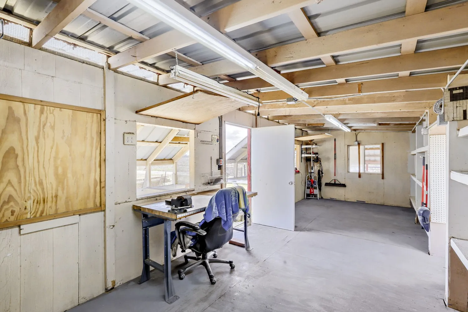 Workshop space featuring exposed wood beam ceiling, concrete flooring, built-in shelving, and multiple windows providing natural light