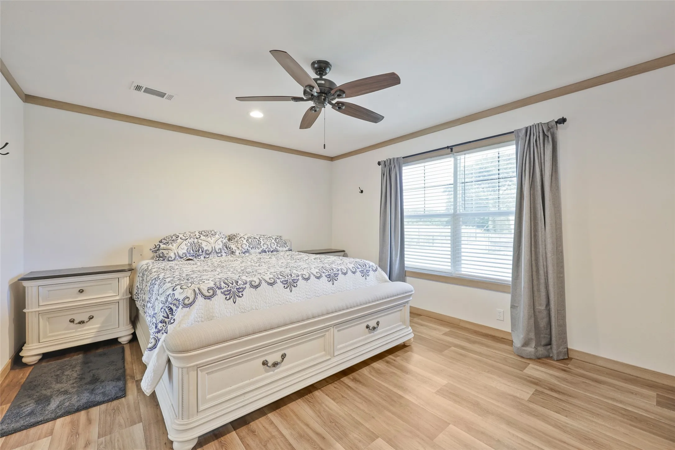 Primary bedroom in 2nd home featuring wood-finish flooring, a window with blinds and drapes, a ceiling fan with integrated lighting, and crown molding