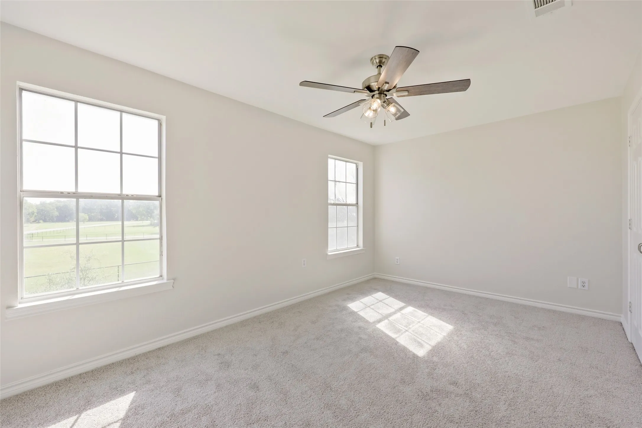 Bright and airy bedroom featuring abundant natural light from dual windows, neutral carpeting, ceiling fan with integrated lighting, and clean white walls throughout
