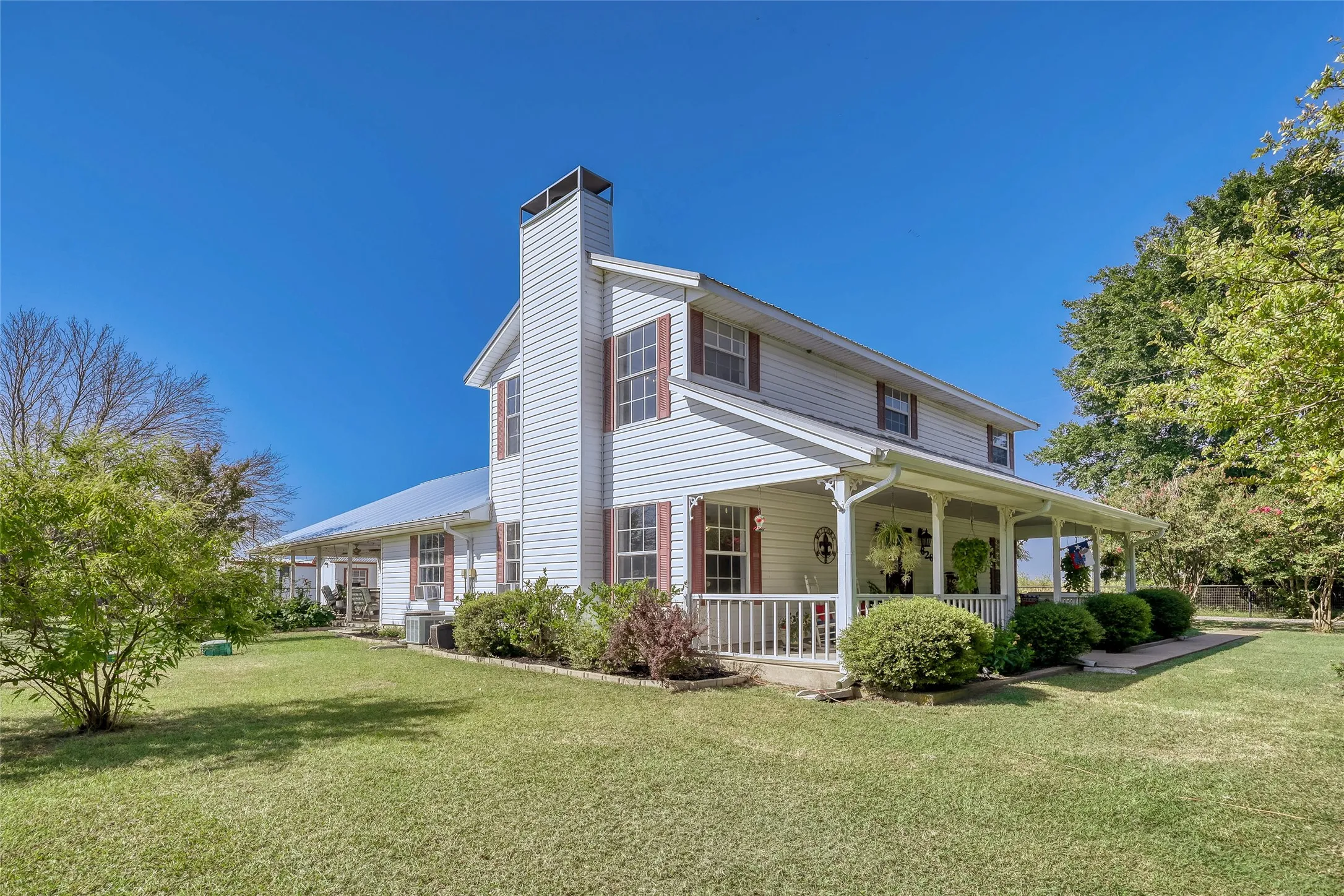 White siding exterior featuring a full-length covered porch with white railing, a prominent chimney, and a metal roof