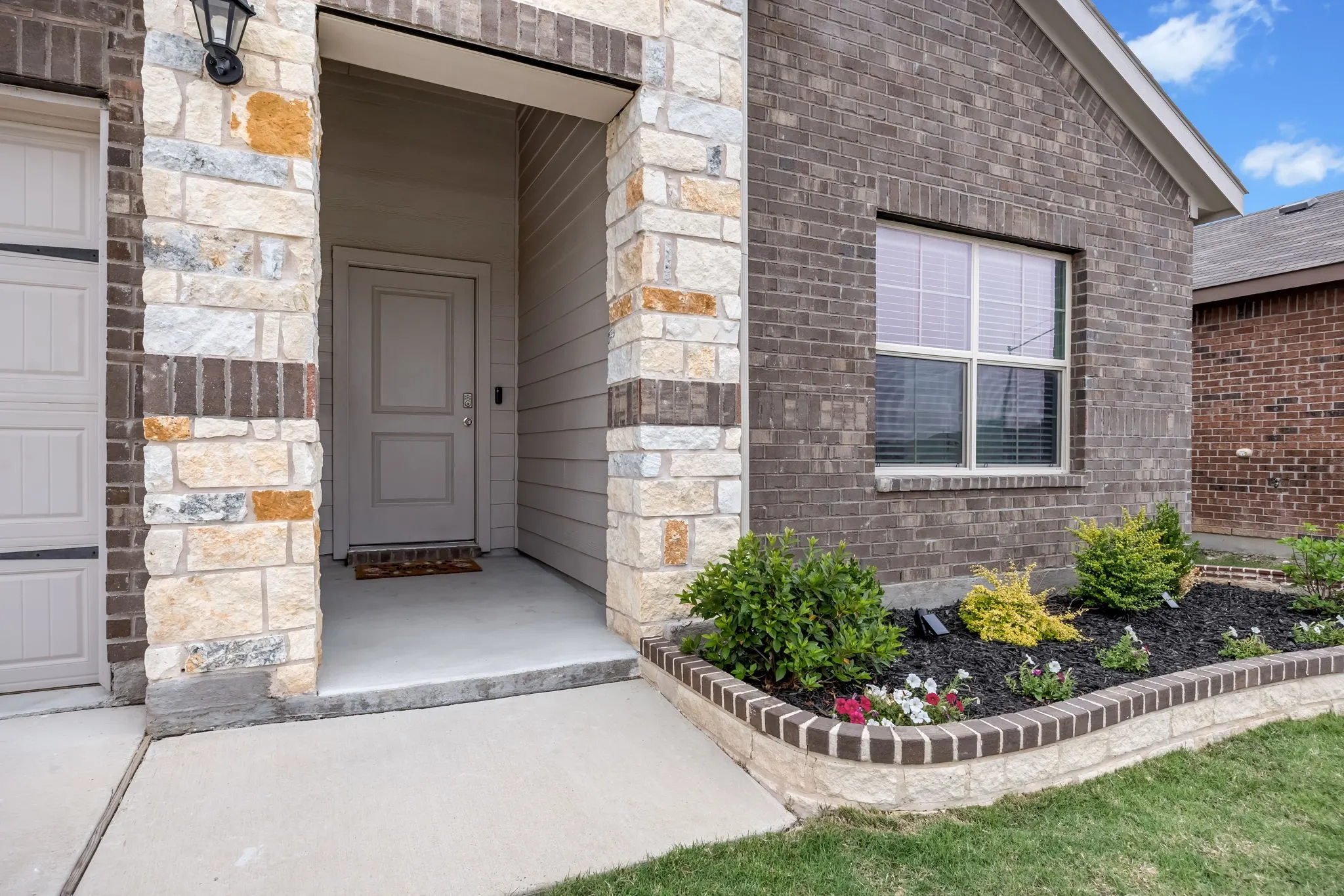 Stone and brick facade featuring a covered entryway, a paneled front door, an exterior light fixture, and a window with blinds