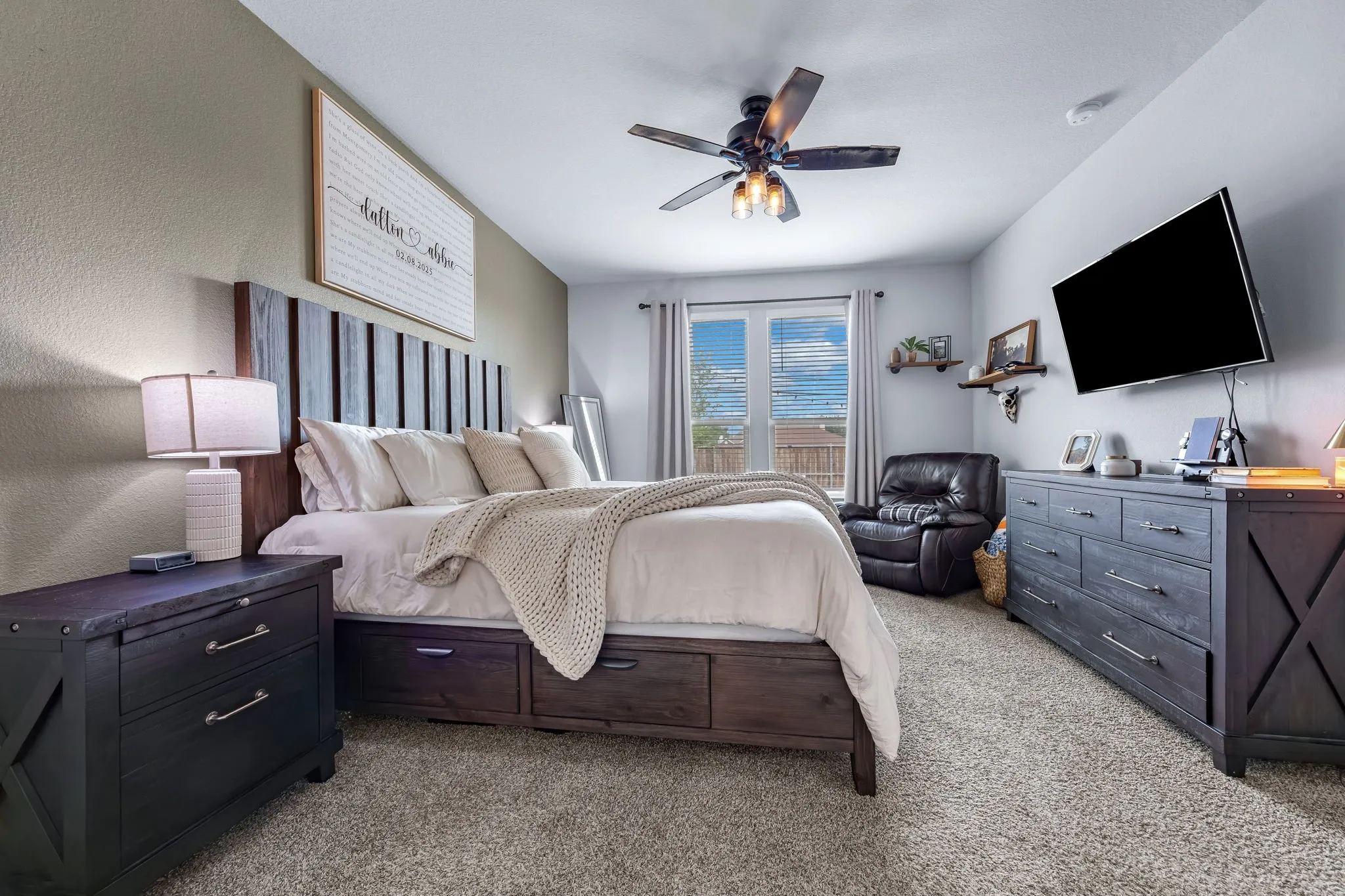 Carpeted bedroom featuring a ceiling fan with integrated lighting, a dark wood-finish bed frame with built-in storage, and two-tone wall paint