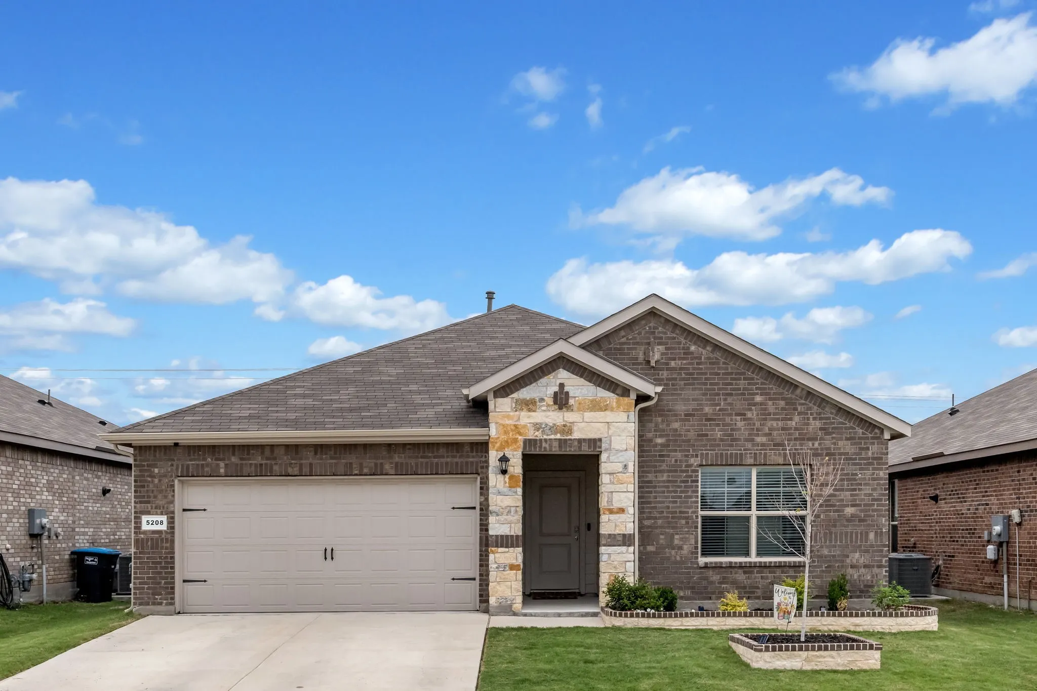 Brick and stone facade residence featuring an attached garage, a covered entry, a gabled roofline, and front landscaping