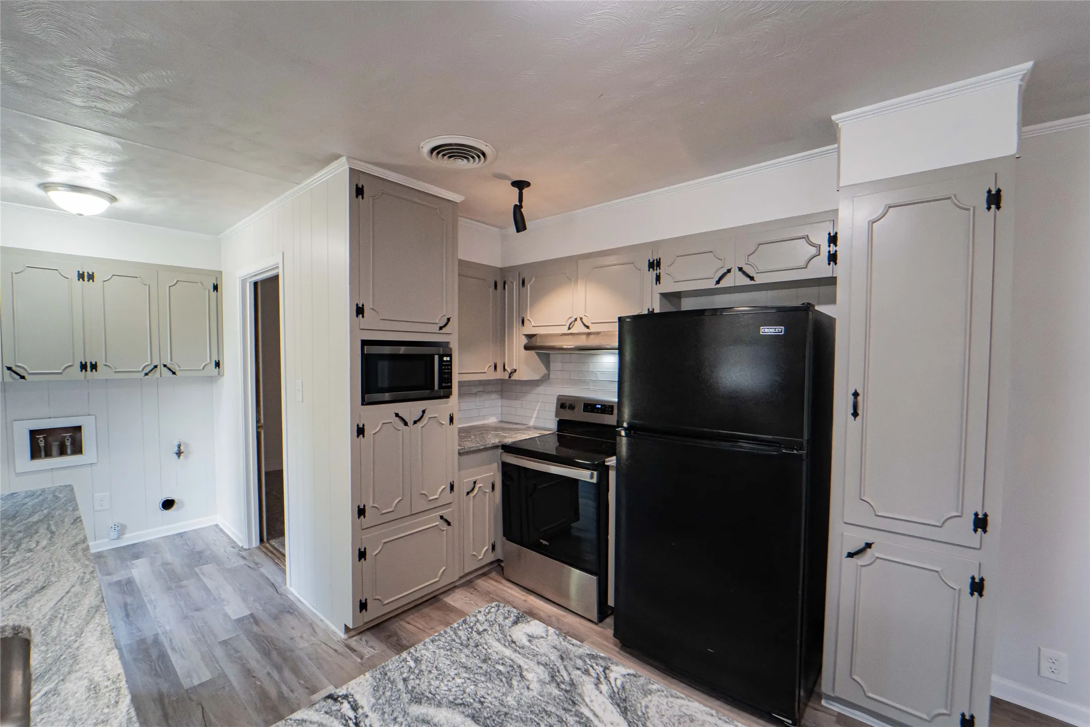 Kitchen featuring wood-finish flooring, light-toned cabinetry with dark hardware, gorgeous stone countertops, and a built-in microwave-conveniently located laundry room adjacent to kitchen.
