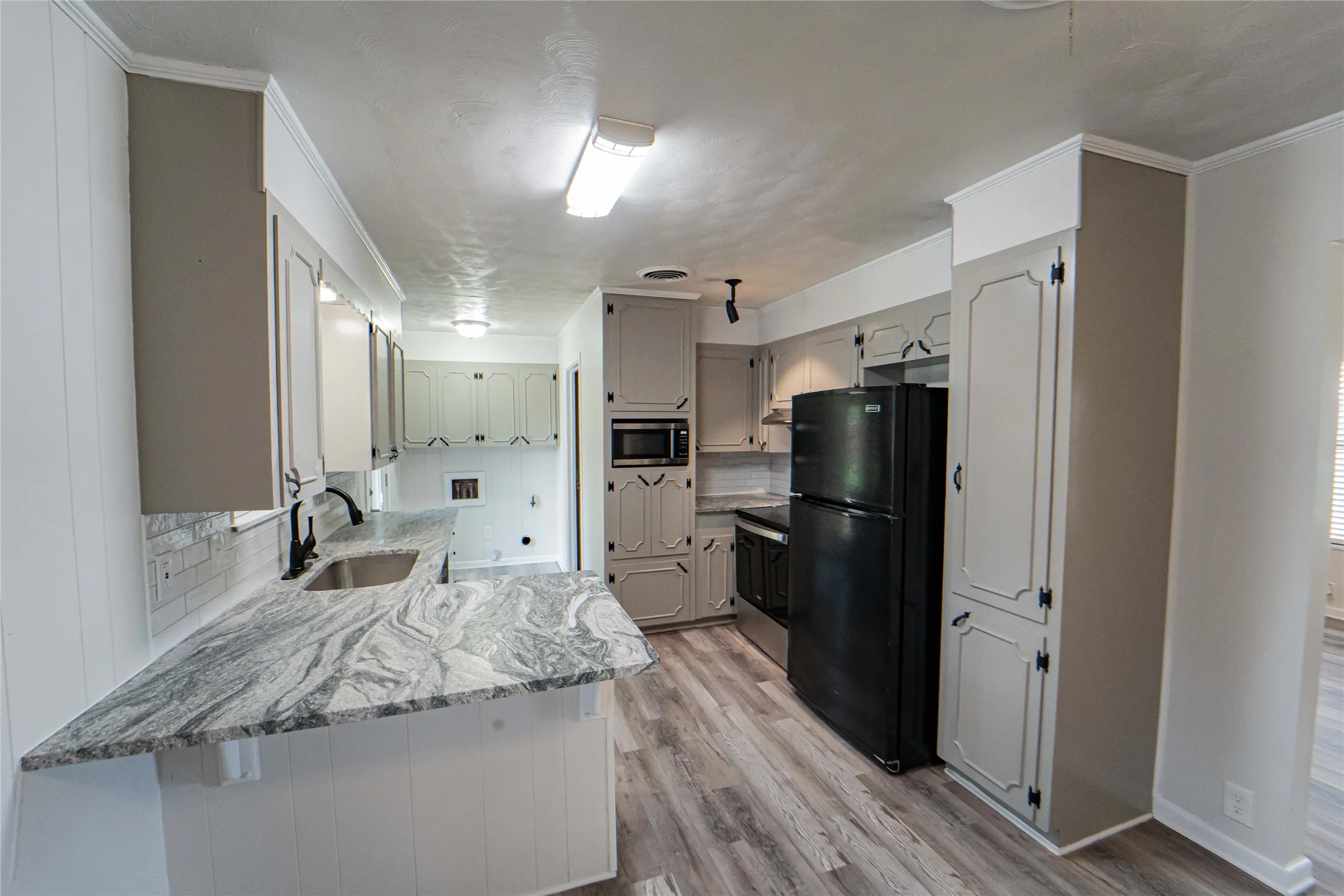 Updated Kitchen featuring wood-finish flooring, ample cabinetry, black appliances, beautiful stone countertops with 'eat-in' breakfast bar, and a white subway tile backsplash