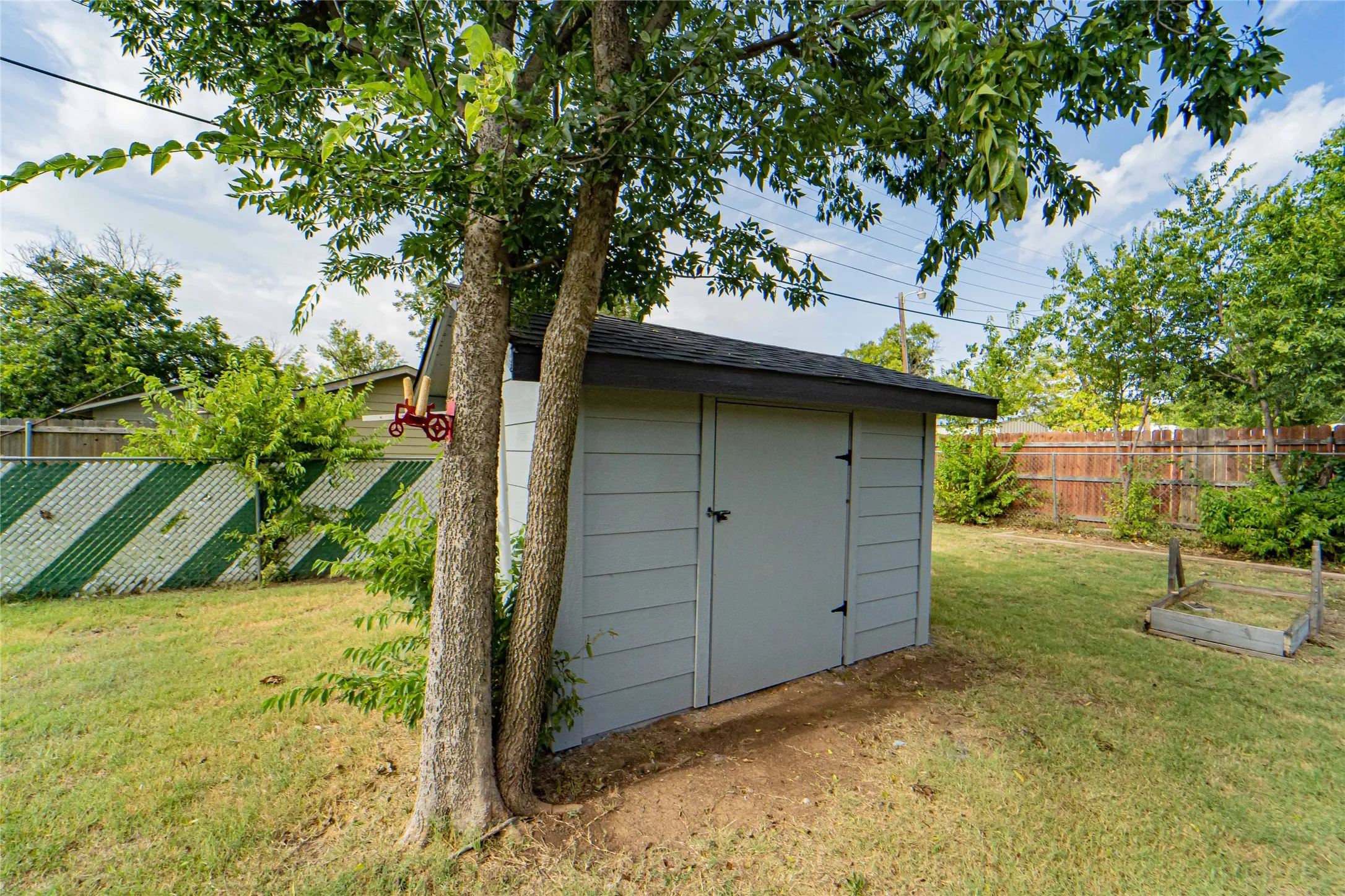 Great workshop/storage building-Backyard features a light gray storage shed with a black shingle roof, surrounded by mature trees