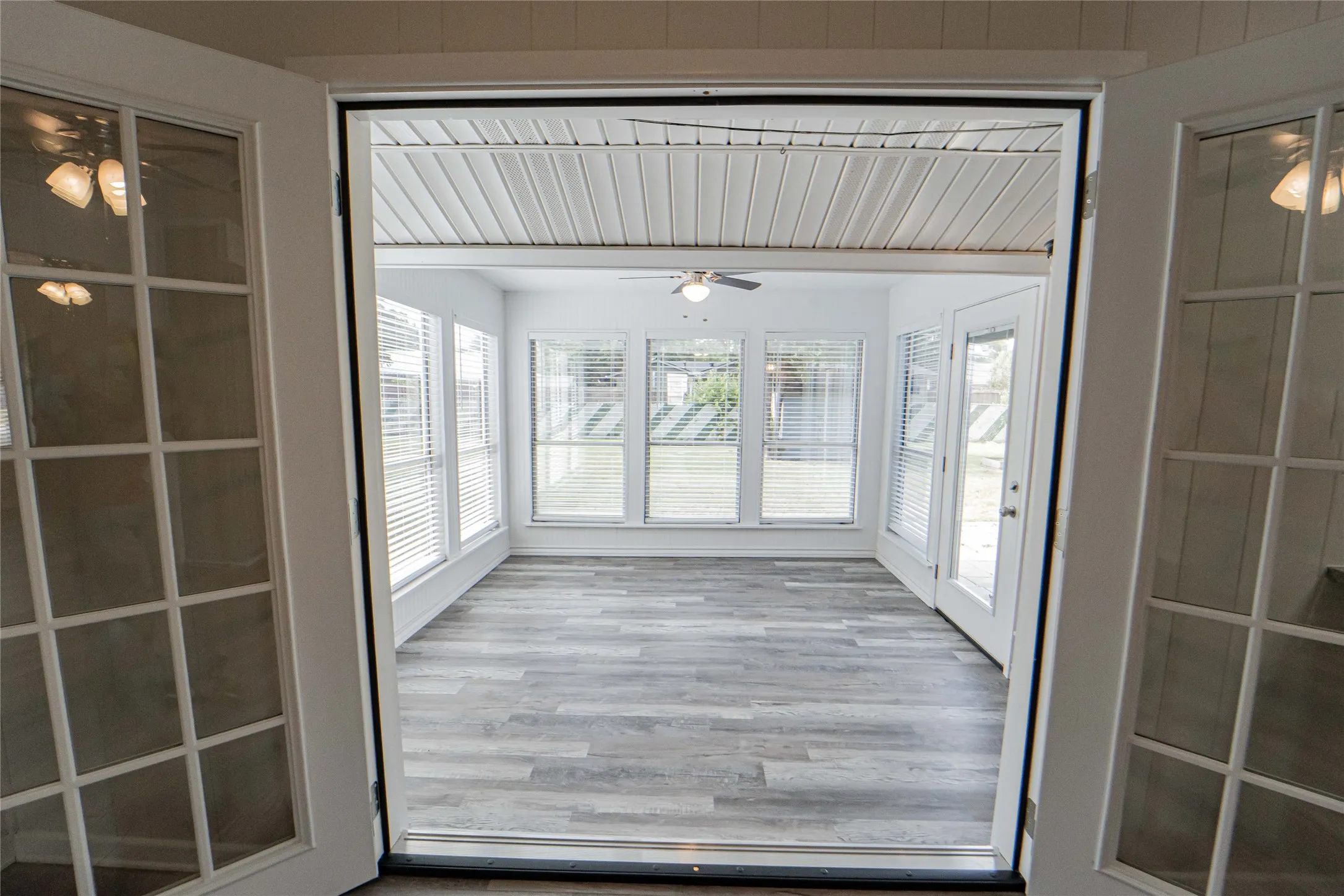 Sunroom featuring open views to a spacious backyard, wood-finish flooring and multiple windows with horizontal blinds
