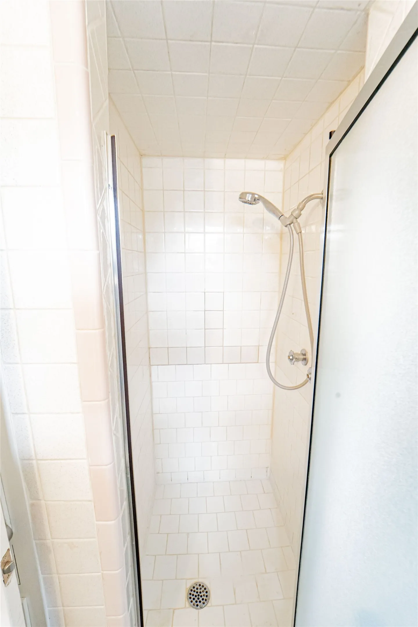 Primary Ensuite-Tiled shower enclosure featuring white subway tile walls and floor, a shower head with an attached sprayer, a metal drain, and a glass shower partition