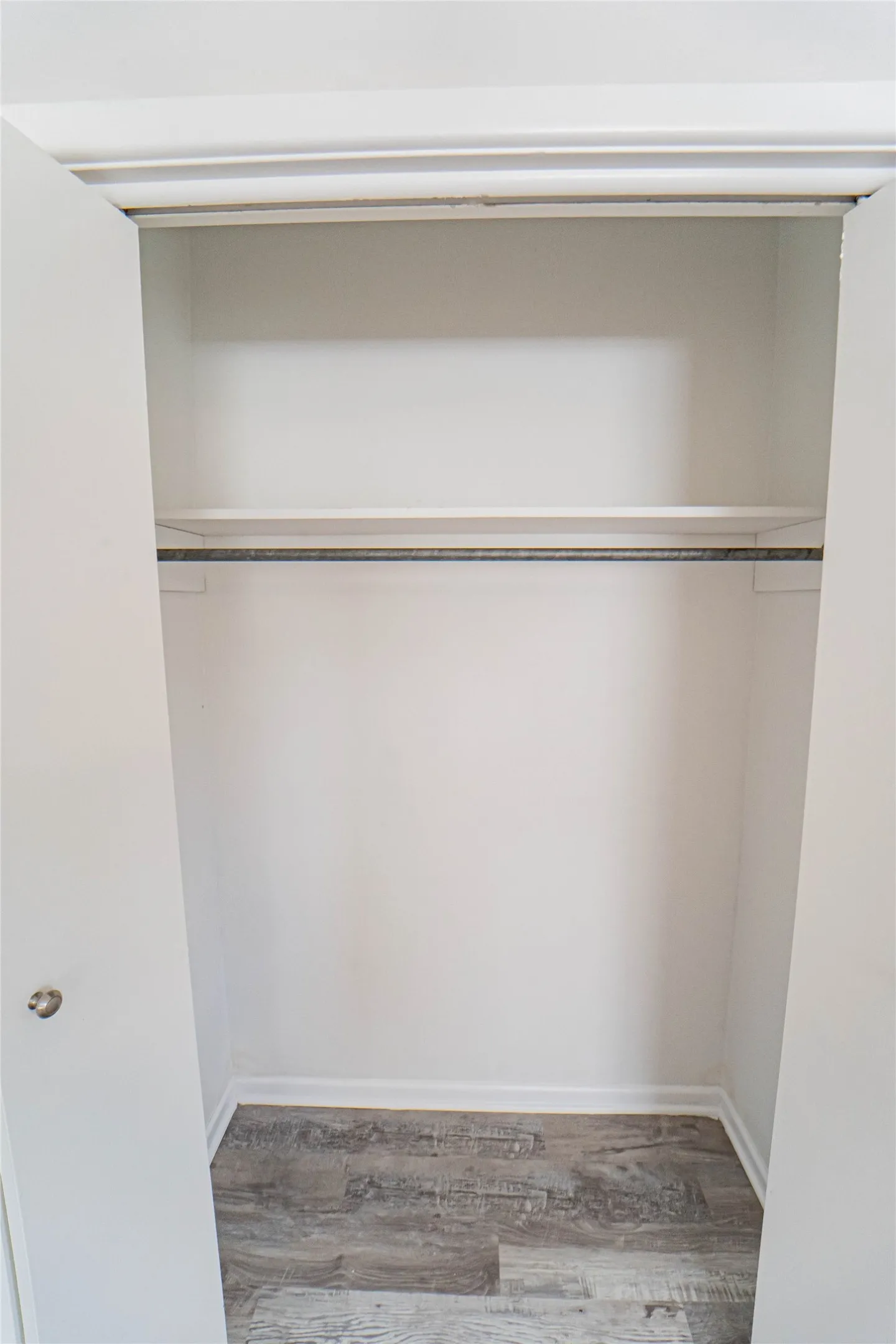 Interior closet featuring a single shelf, hanging rod, and wood-finish flooring-One of the two closets featured in the primary bedroom