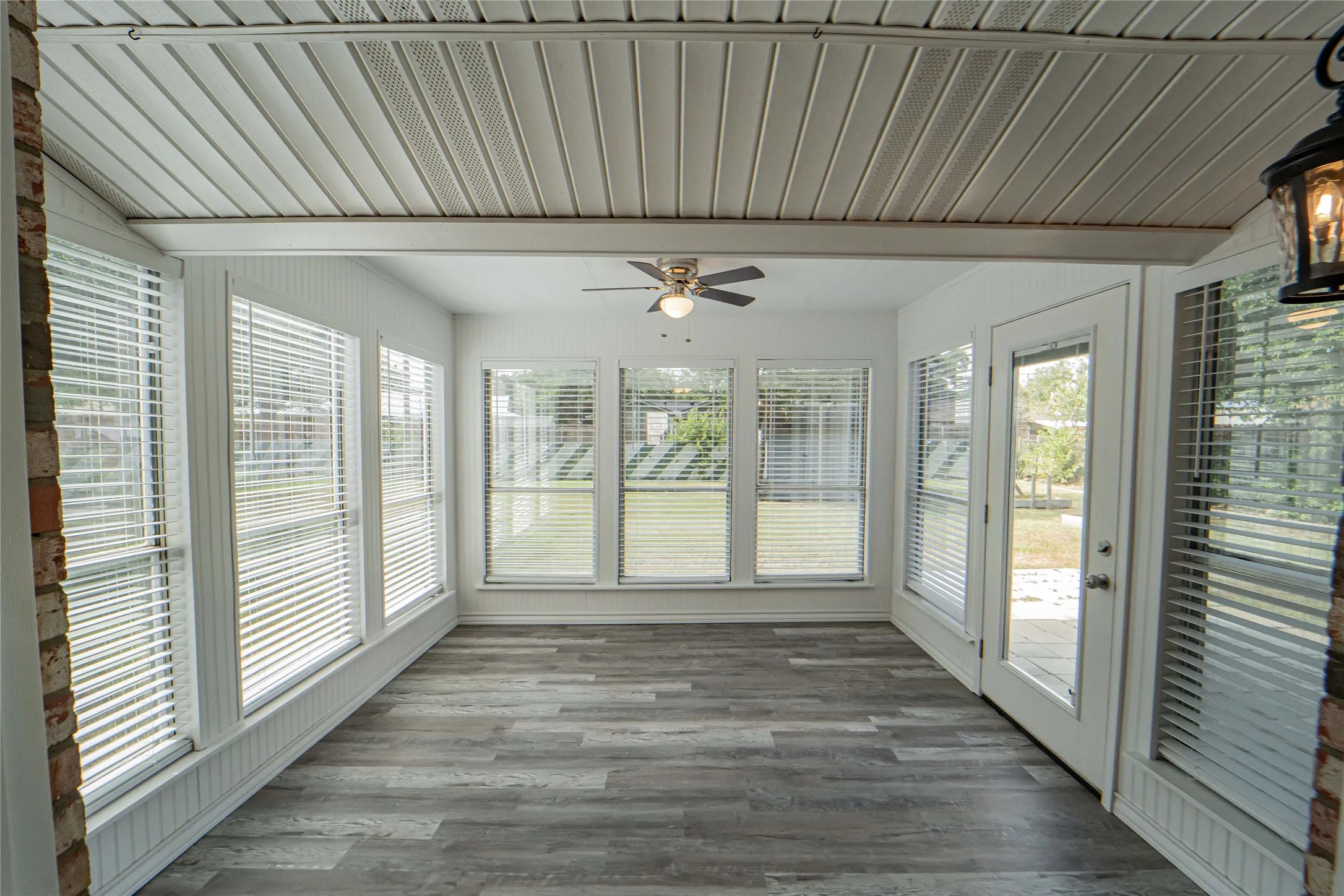 Morning coffee just got better! Enclosed sunroom, located off the dining and kitchen area- featuring wood-finish flooring, a ceiling fan with light fixture, and multiple windows with blinds and open views of the large back yard.