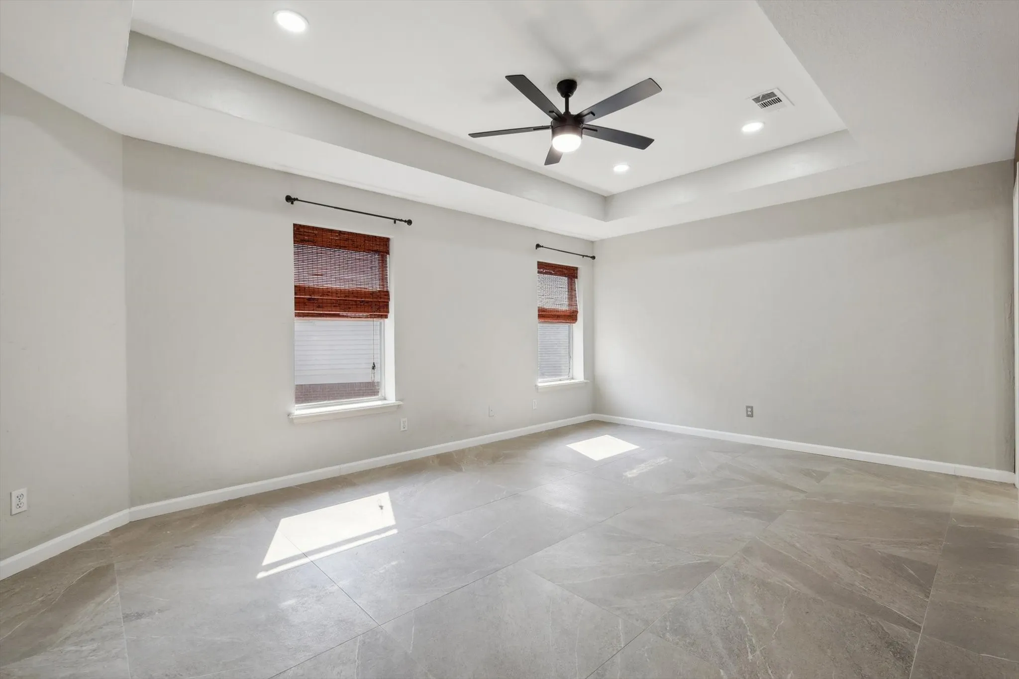 Primary bedroom featuring tile patterned floors, ceiling fan, and a raised ceiling