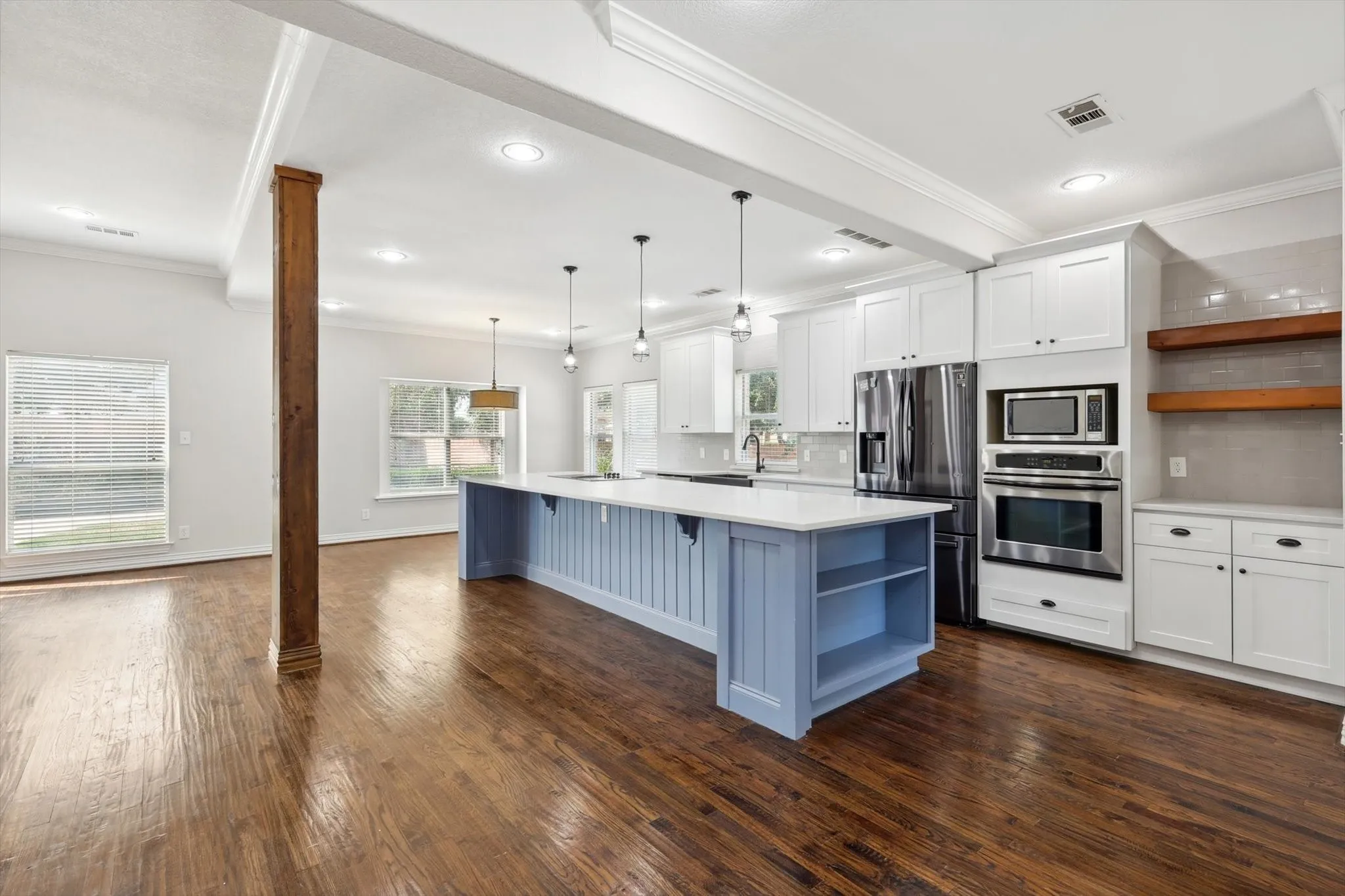Kitchen with stainless steel appliances, dark hardwood / wood-style flooring, pendant lighting, white cabinetry, and a center island.