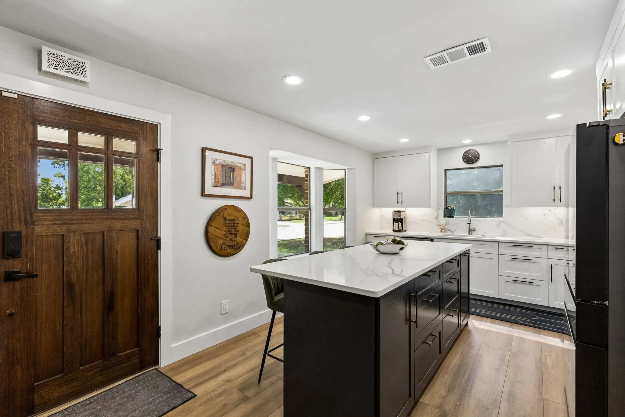 Kitchen featuring white cabinetry, a dark island with a white countertop, stainless steel sink, and wood-finish flooring
