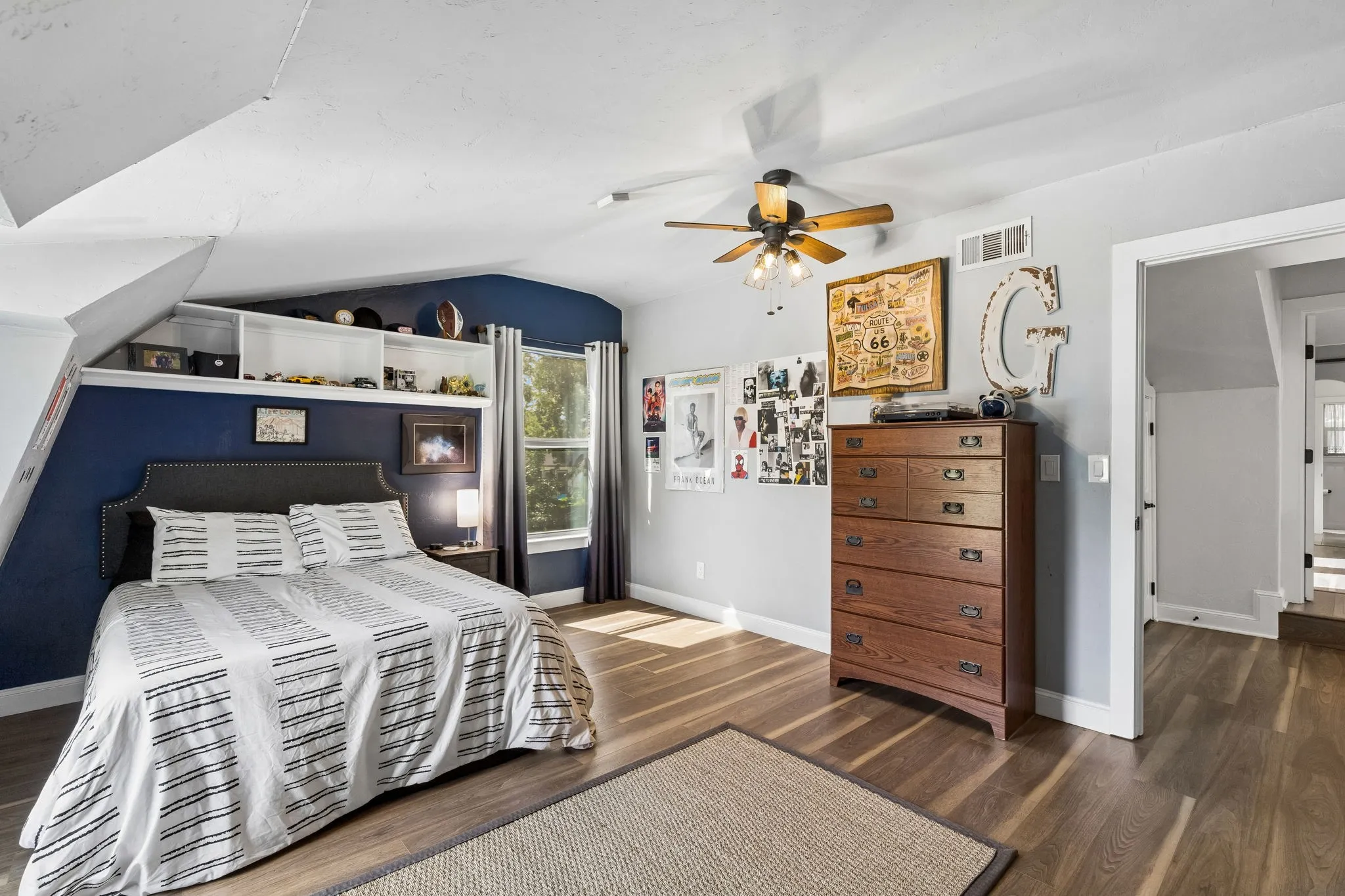 Secondary bedroom featuring wood-finish flooring, a ceiling fan with integrated lighting, built-in shelving, a window with natural light, and a framed doorway opening to an additional interior space