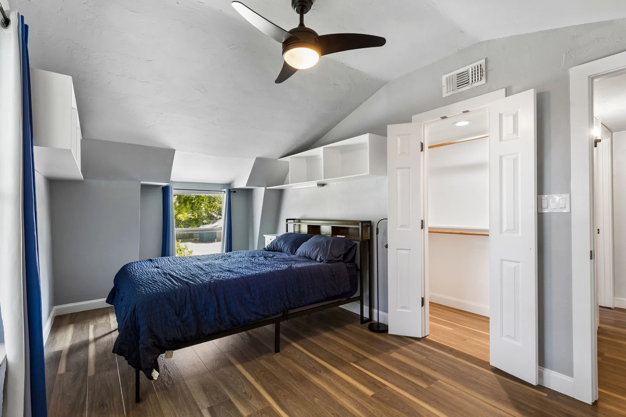 Hardwood-finish flooring featuring a built-in closet with bifold doors, an overhead ceiling fan, and built-in shelving