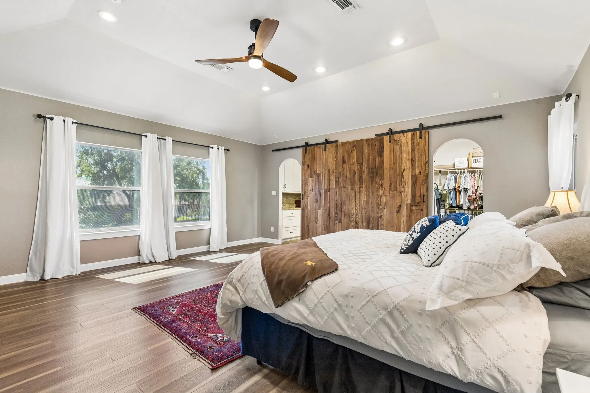 Vaulted ceiling featuring a ceiling fan with integrated lighting, wood-finish flooring, and dual windows