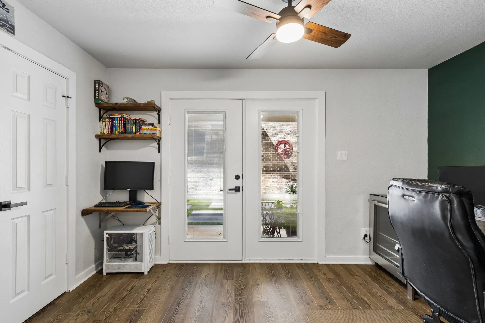 Bright interior space featuring wood-finish flooring, a ceiling fan with integrated lighting, and a white paneled door