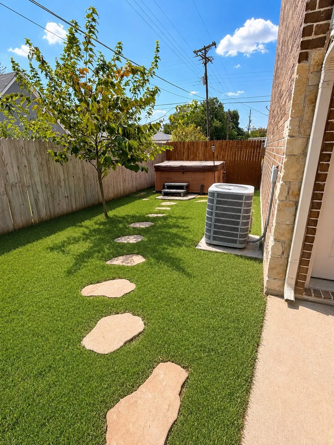 Compact backyard featuring a wood-panel fence, stone paver pathway, and a hot tub
