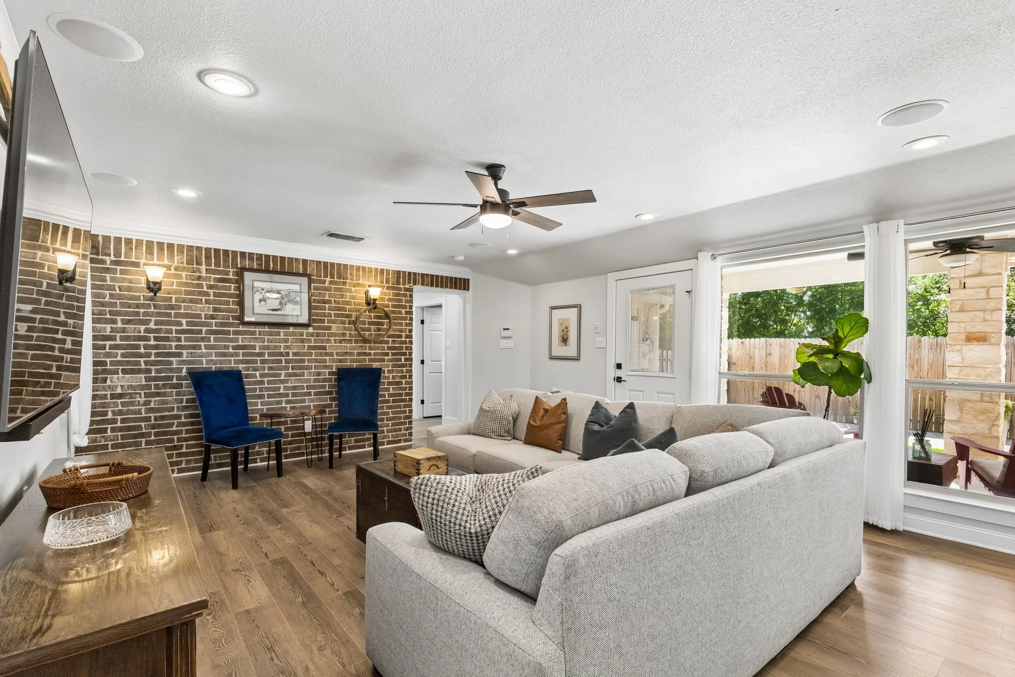 Spacious living area featuring a prominent exposed brick accent wall, recessed lighting, and wood-finish flooring
