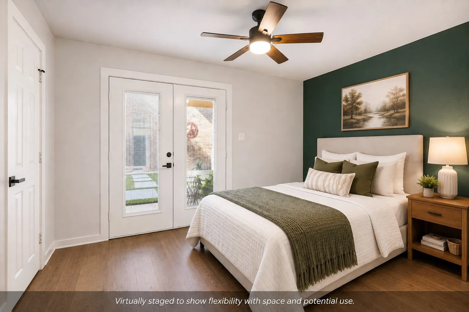 Wood-finish flooring, ceiling fan with integrated lighting, a dedicated accent wall, and double glass-paneled doors with direct access to a paved outdoor area