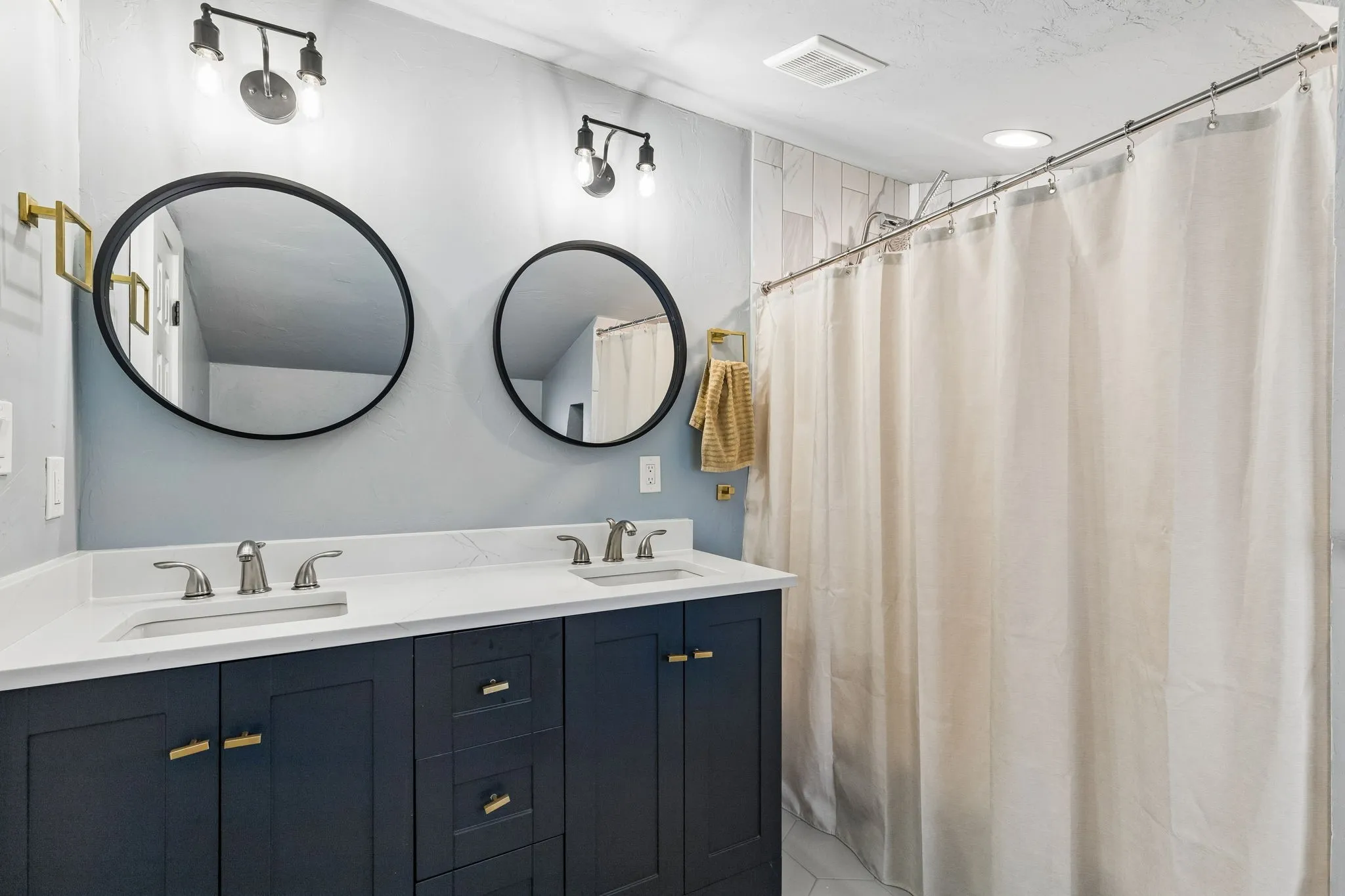 Dual vanity featuring a white countertop, undermount sinks, and dark cabinetry with gold-tone hardware