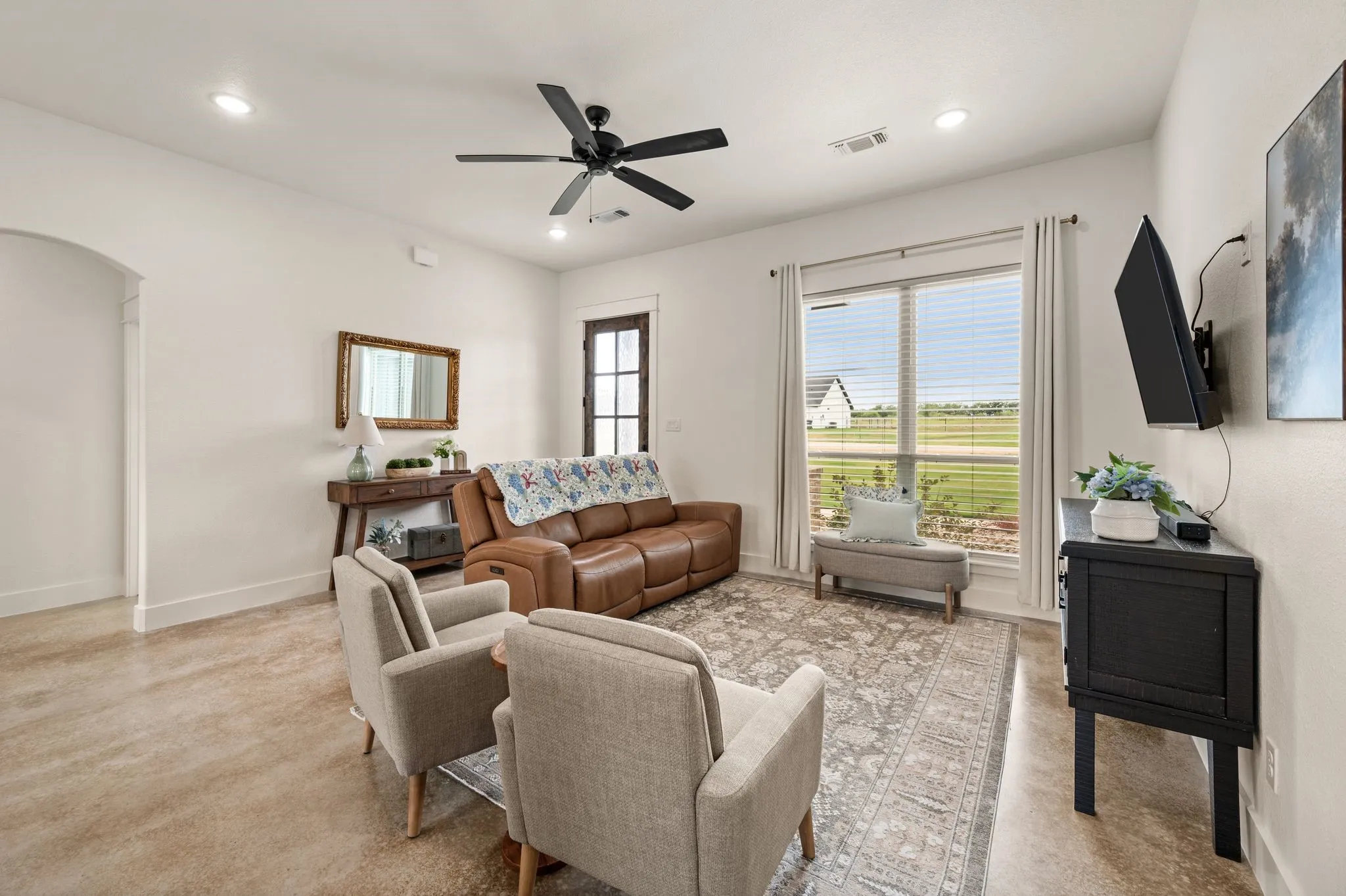 Spacious living area featuring polished concrete flooring, recessed lighting, a modern ceiling fan, and large windows with blinds for natural light