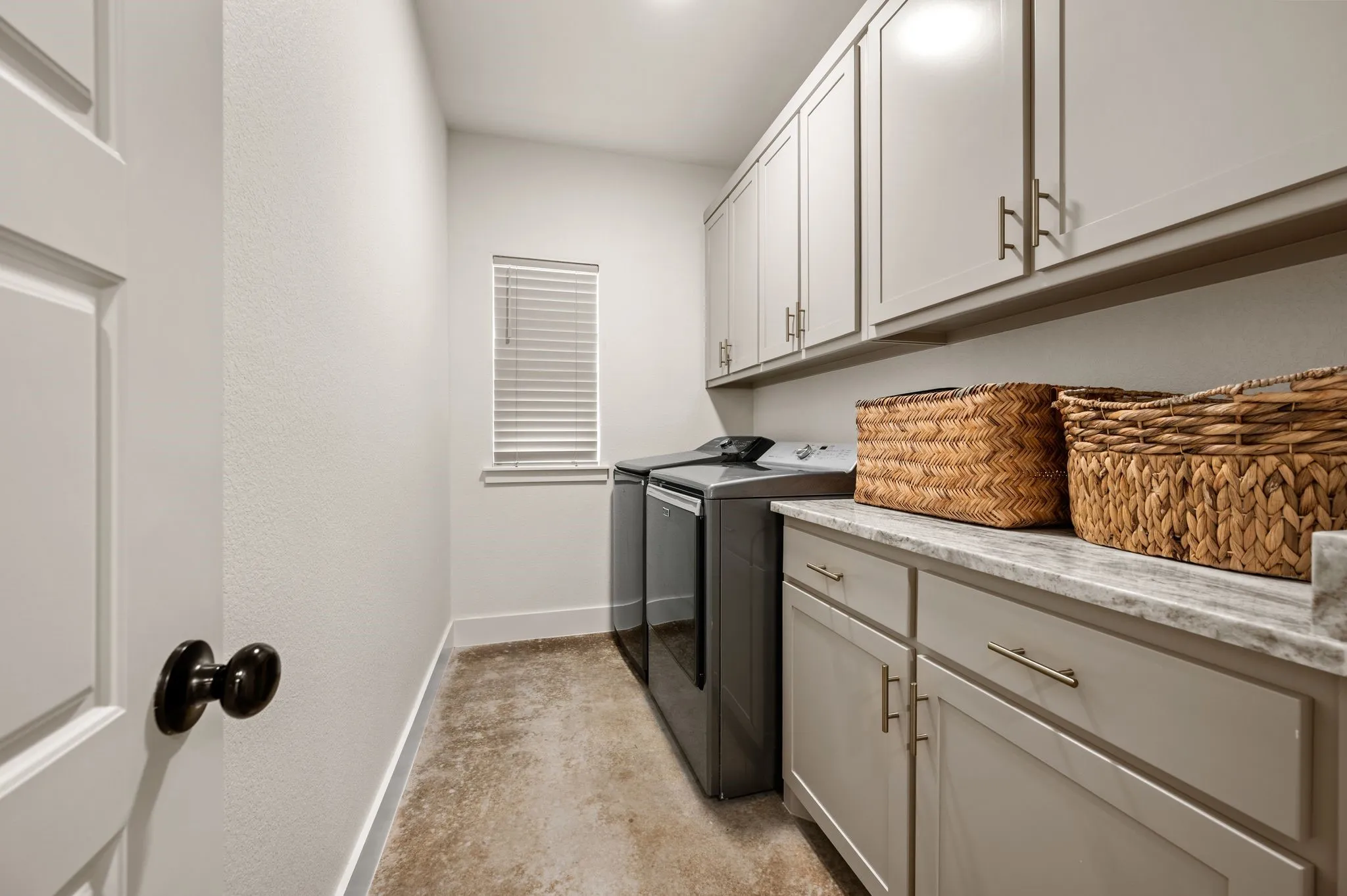 Dedicated utility room featuring upper and lower cabinetry, a light-toned countertop, and a window with blinds