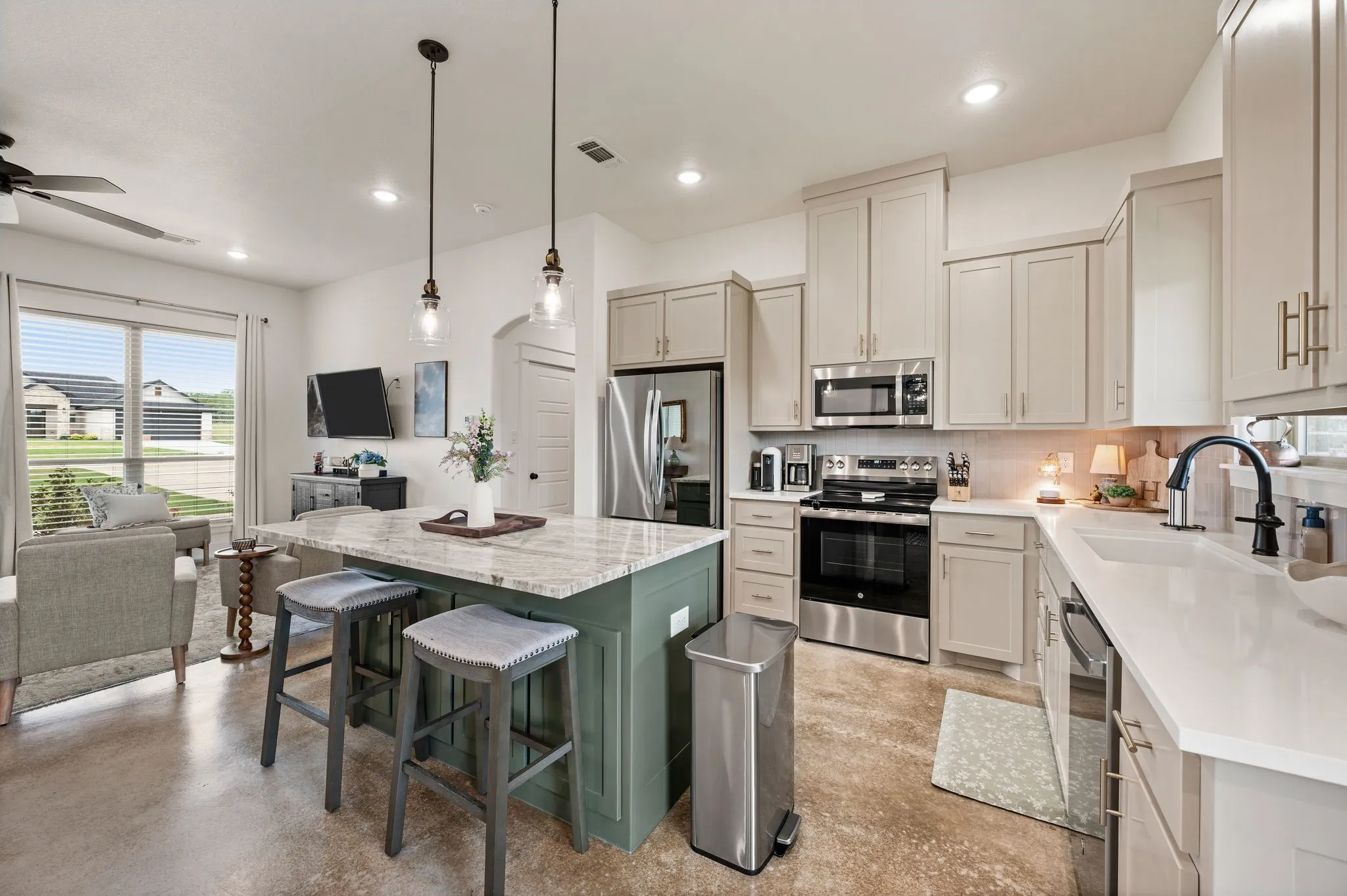 Open-concept kitchen featuring an island with counter seating, light-colored cabinetry, stainless steel appliances, and a tile backsplash