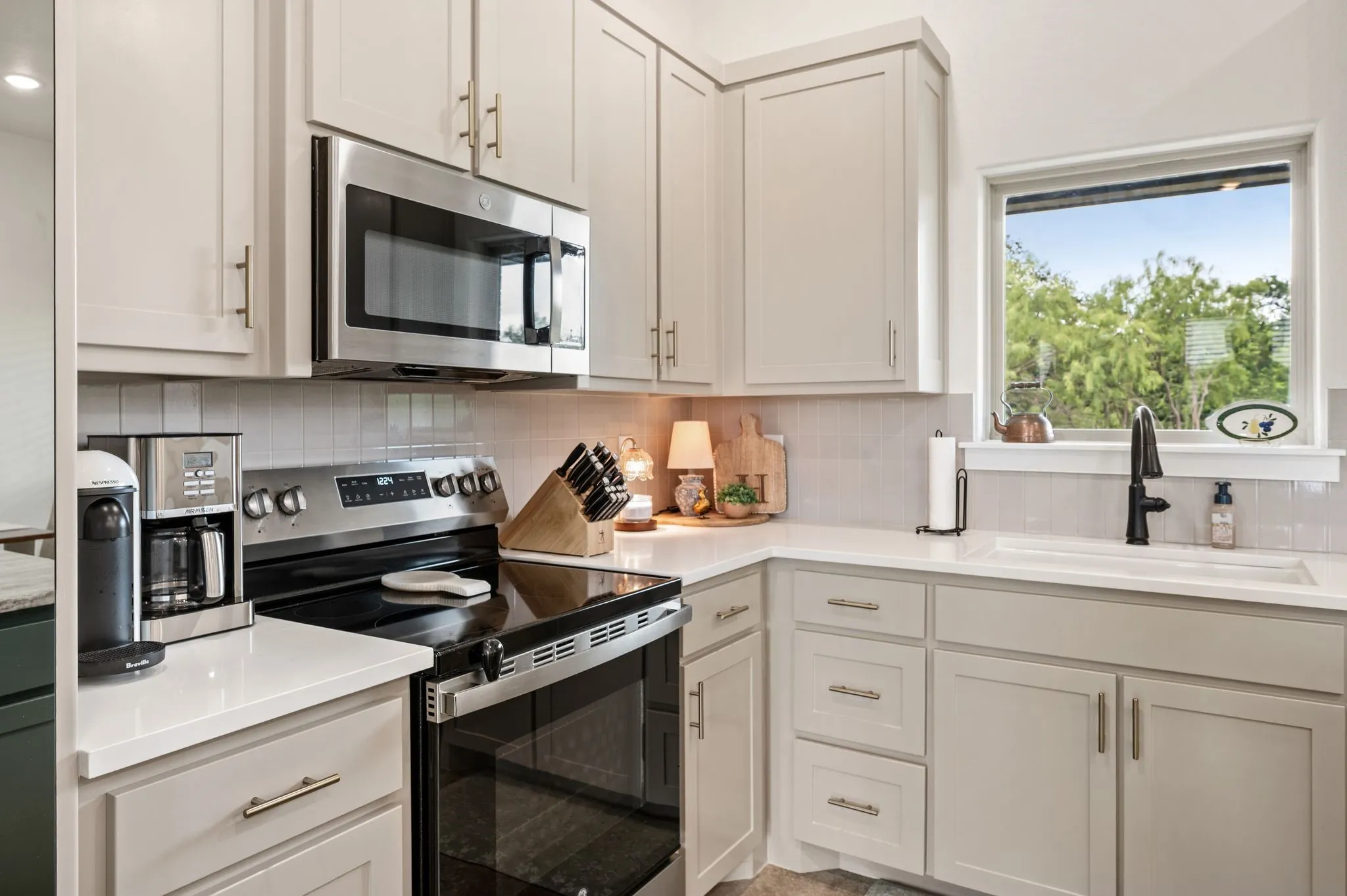 Kitchen featuring light-toned cabinetry, stainless steel appliances, a white subway tile backsplash, and light-toned countertops