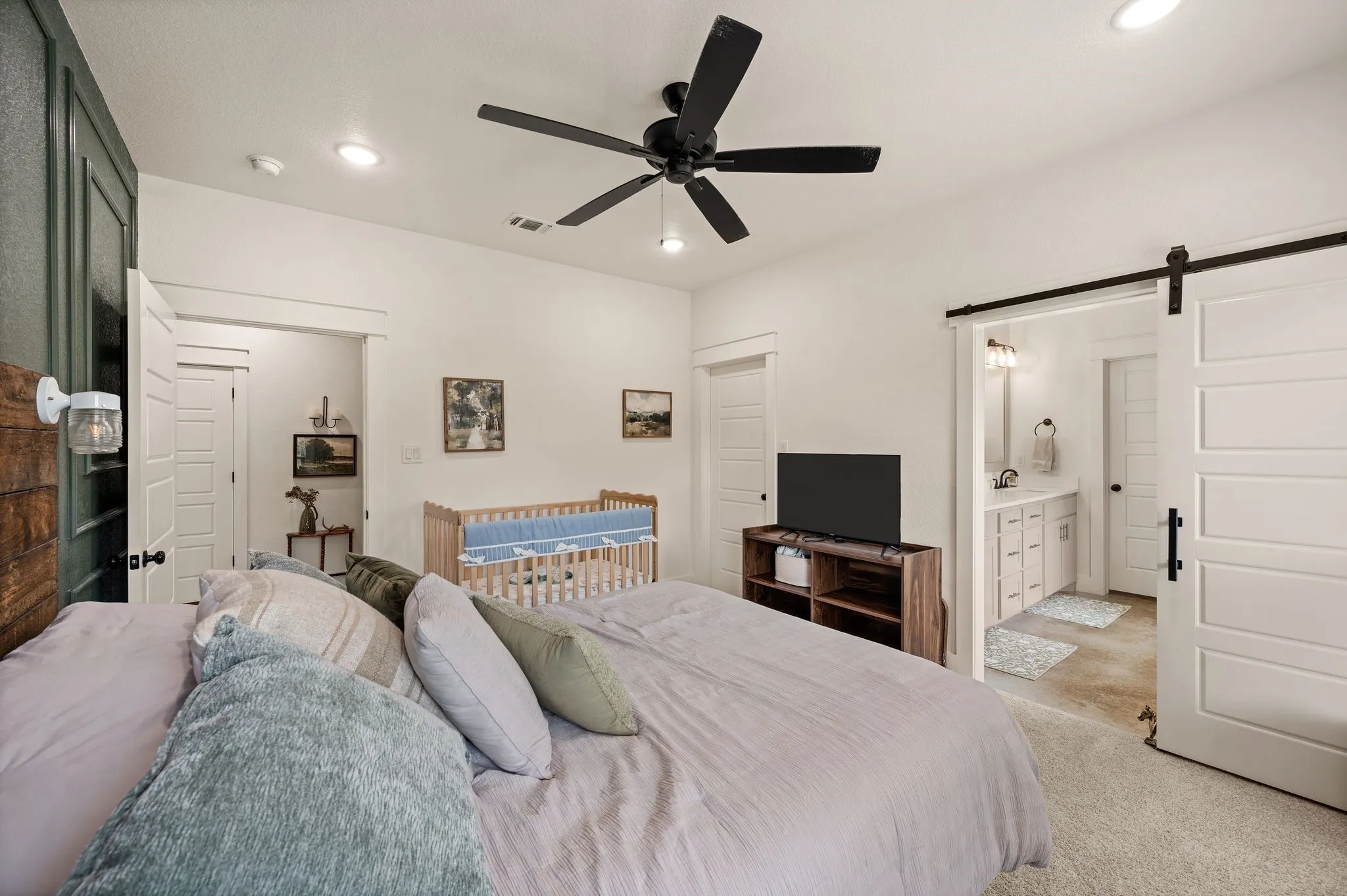 White walls featuring a black ceiling fan, recessed lighting, and a white barn door leading to a bathroom with a dual vanity