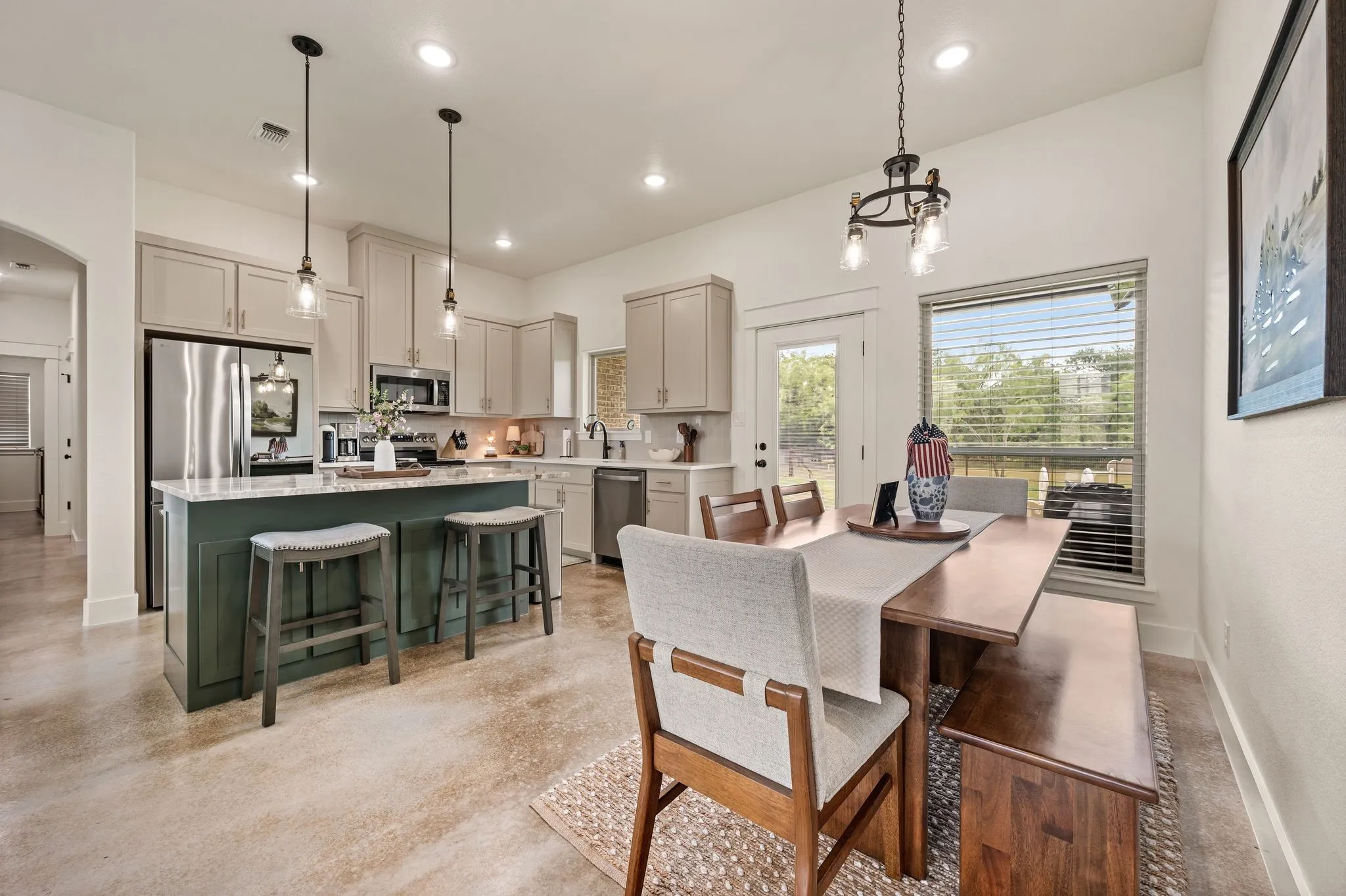 Open-concept kitchen and dining area featuring a central island with seating, stainless steel appliances, light-toned cabinetry, and concrete-finish flooring