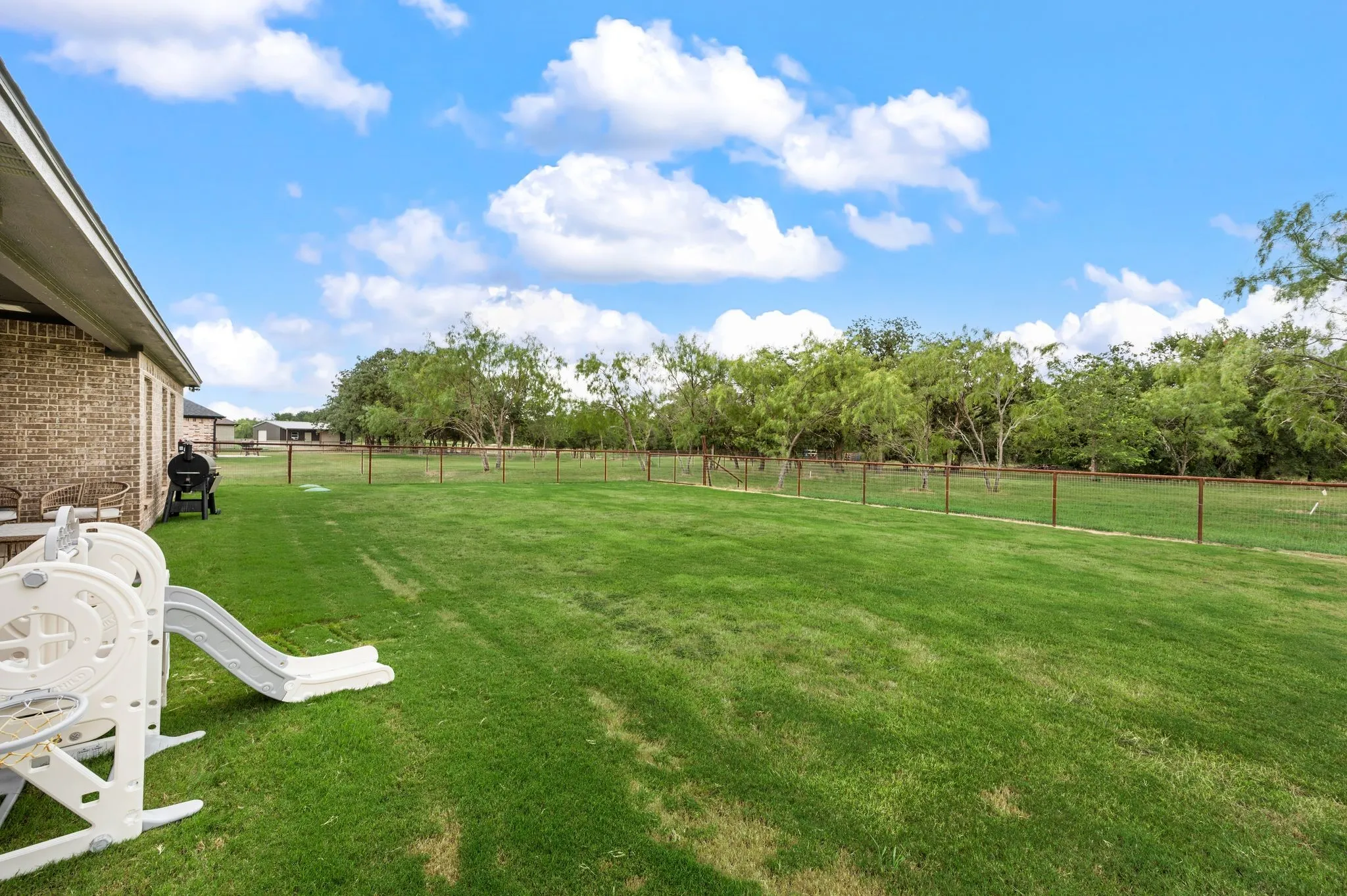 Expansive grass lawn bordered by a metal post fence and mature trees